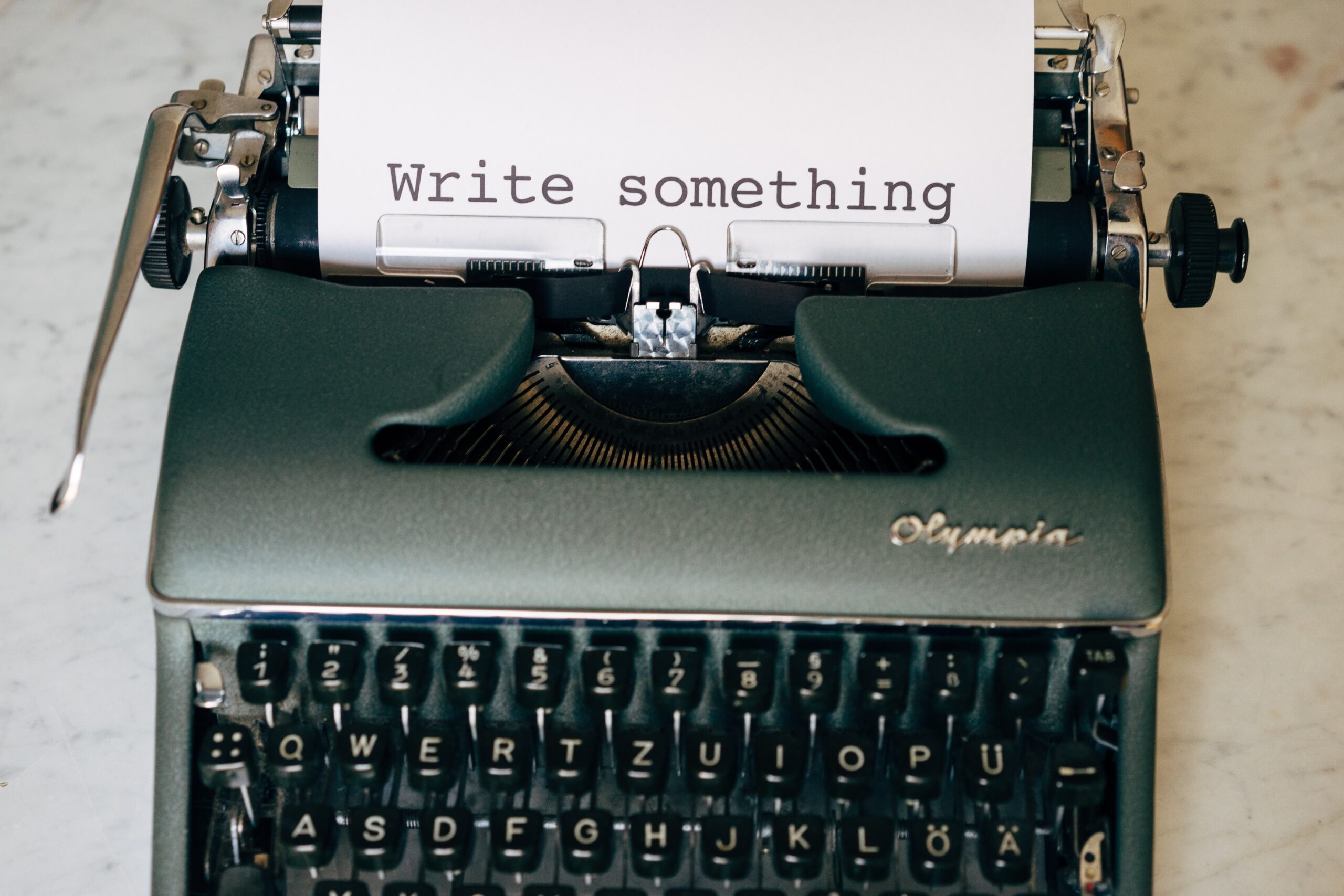 Dark green type writer with "write something" typed onto the page