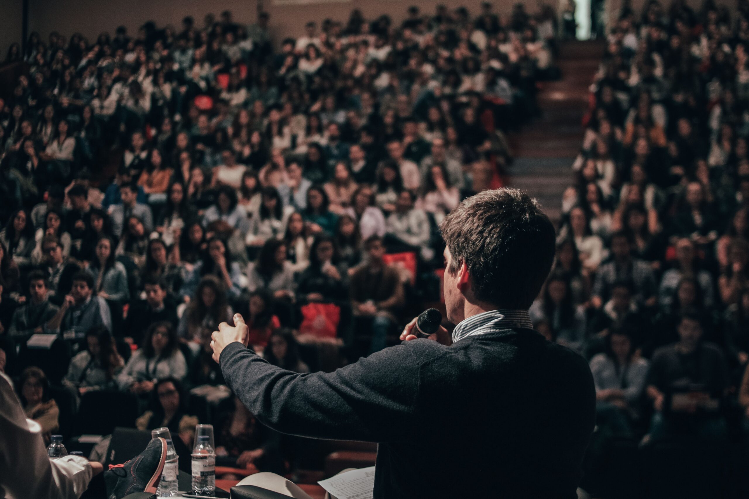 A man holding a microphone faces a large crowd.