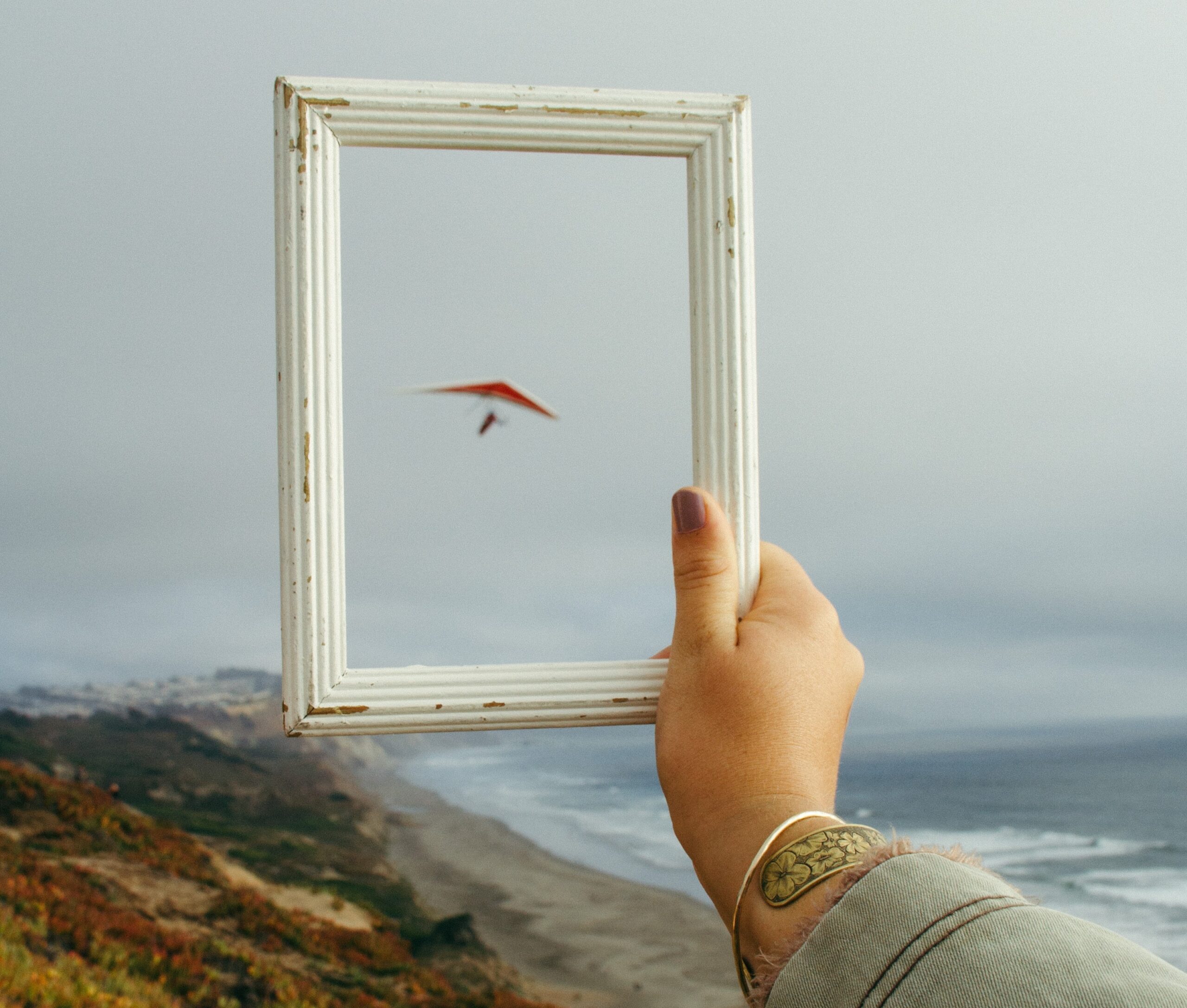 Person holding rectangular white frame standing on a rock