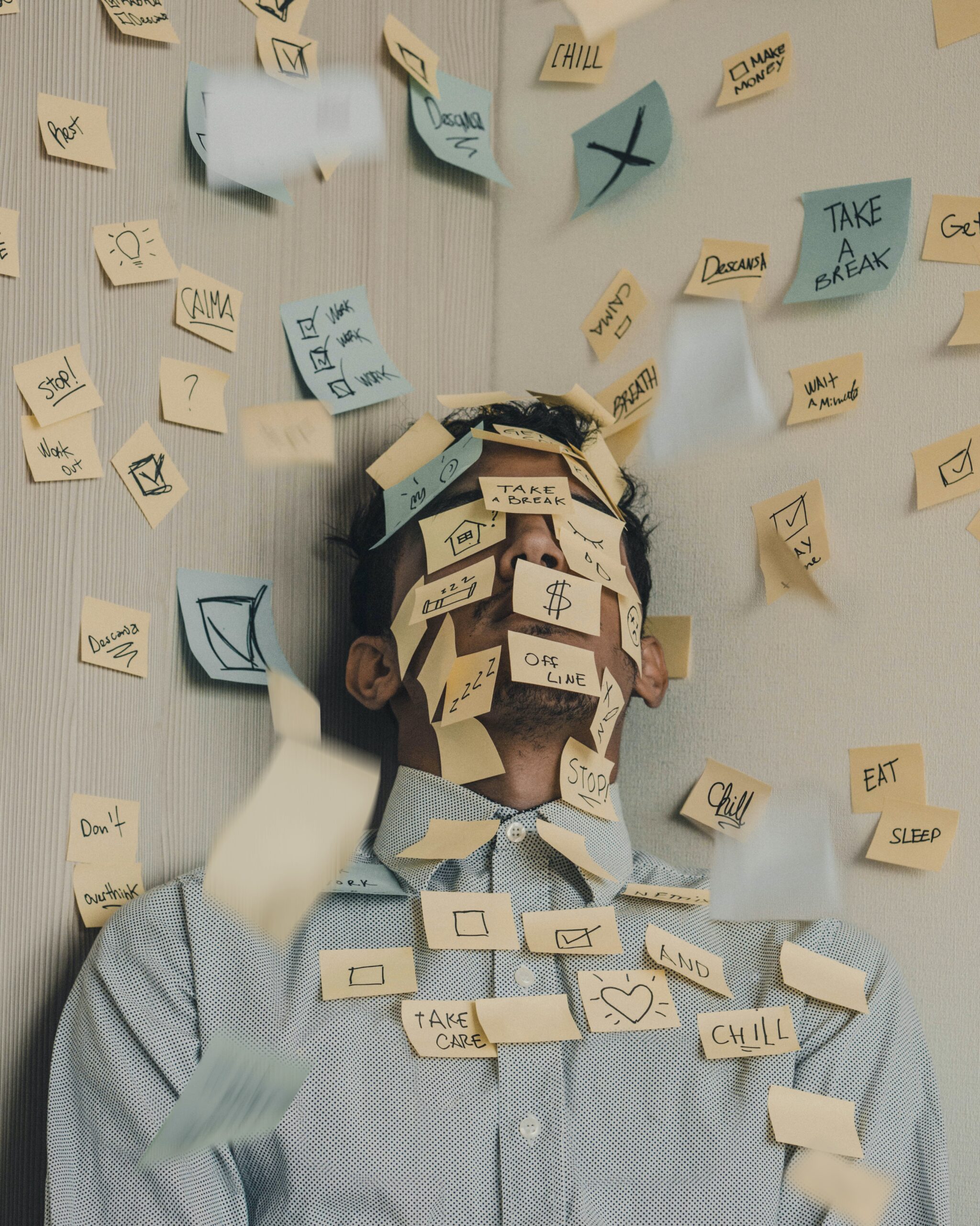 A man in a blue button up shirt sits back, surrounded by post it notes, many of which cover his face and chest.