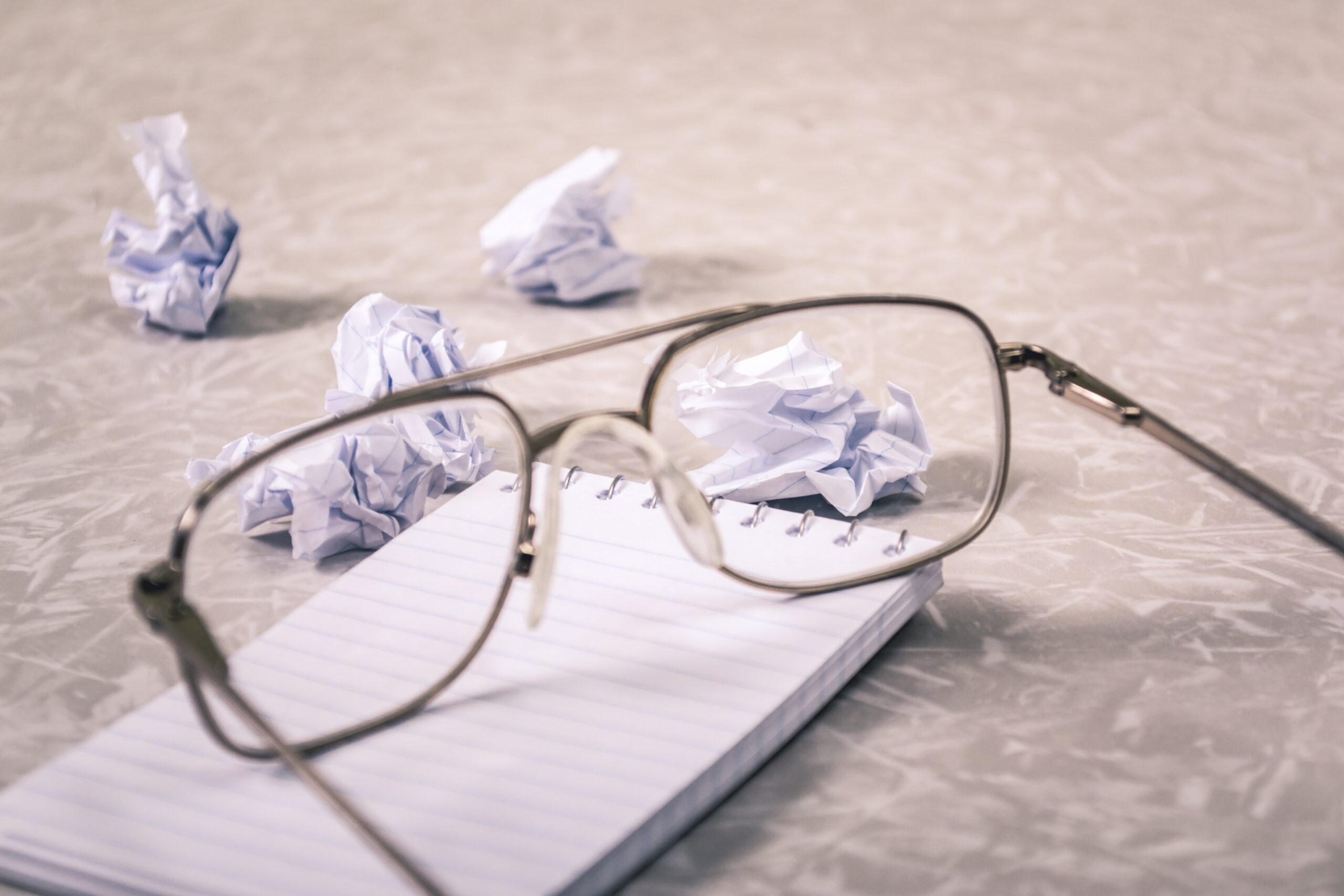 glasses and crumbled paper on top of note pad.