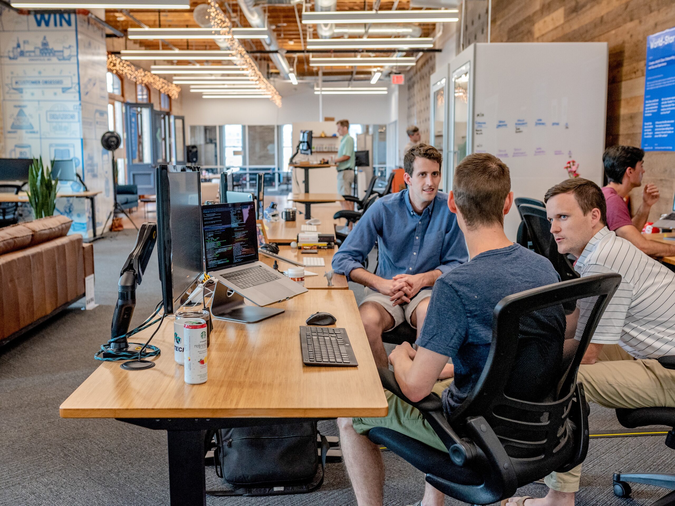 3 men sit at a computer desk having a conversation.