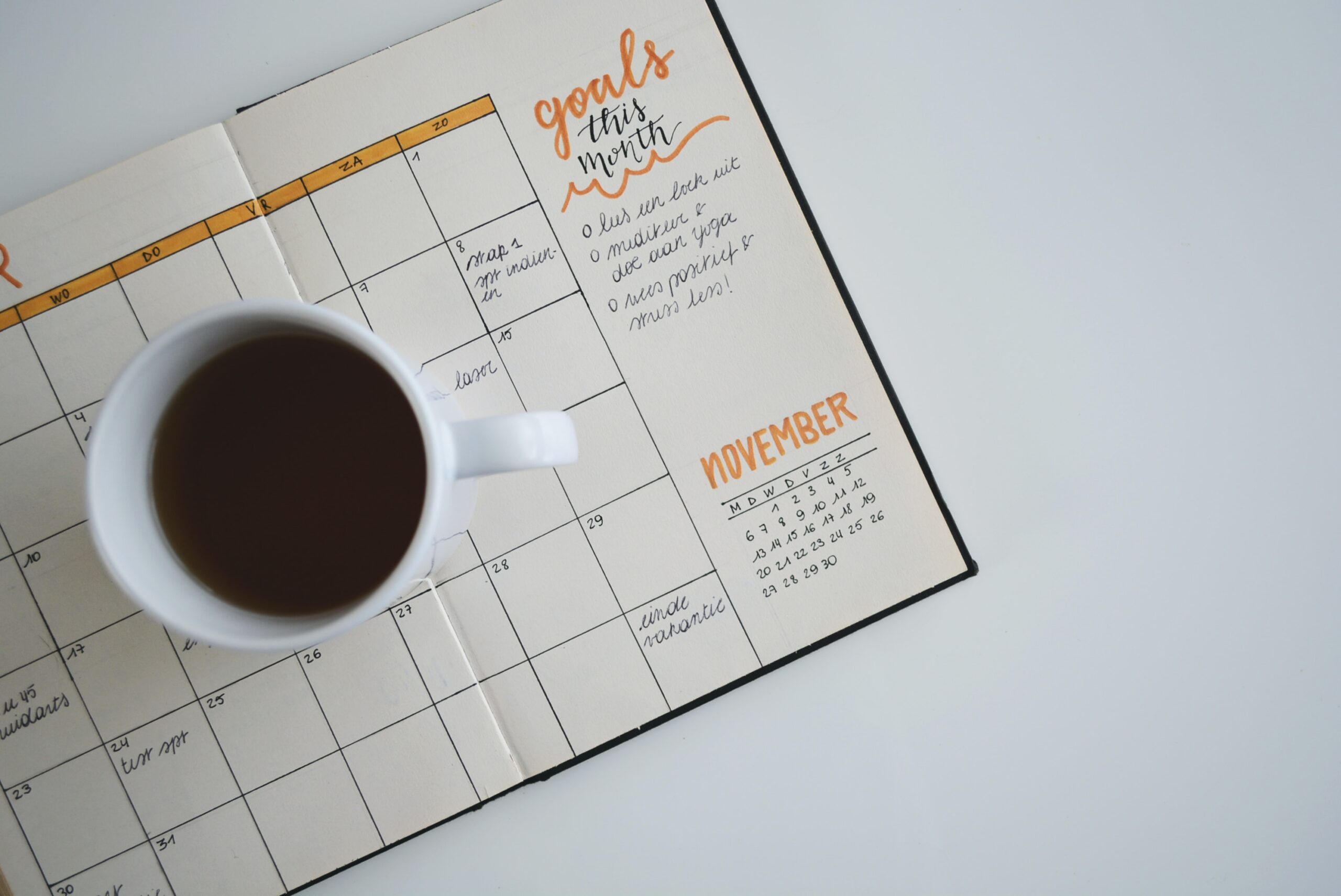 white ceramic mug with coffee on top of planner