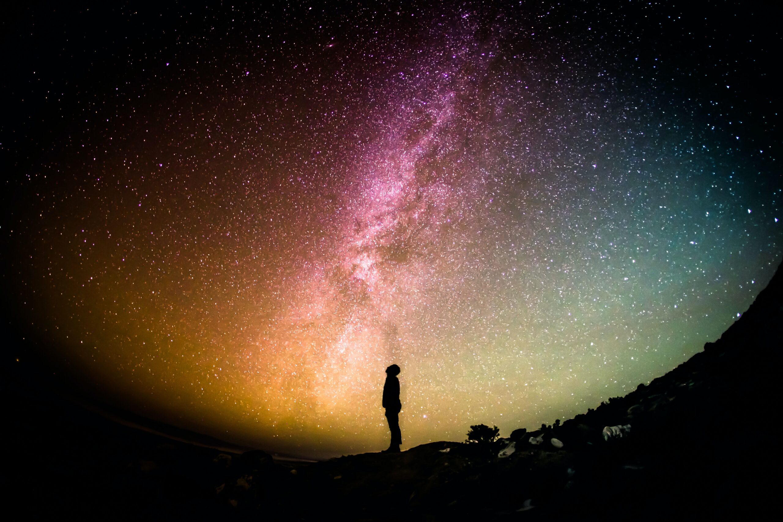 A silhouetted person looks up at the night sky. It is colorful and full of stars.