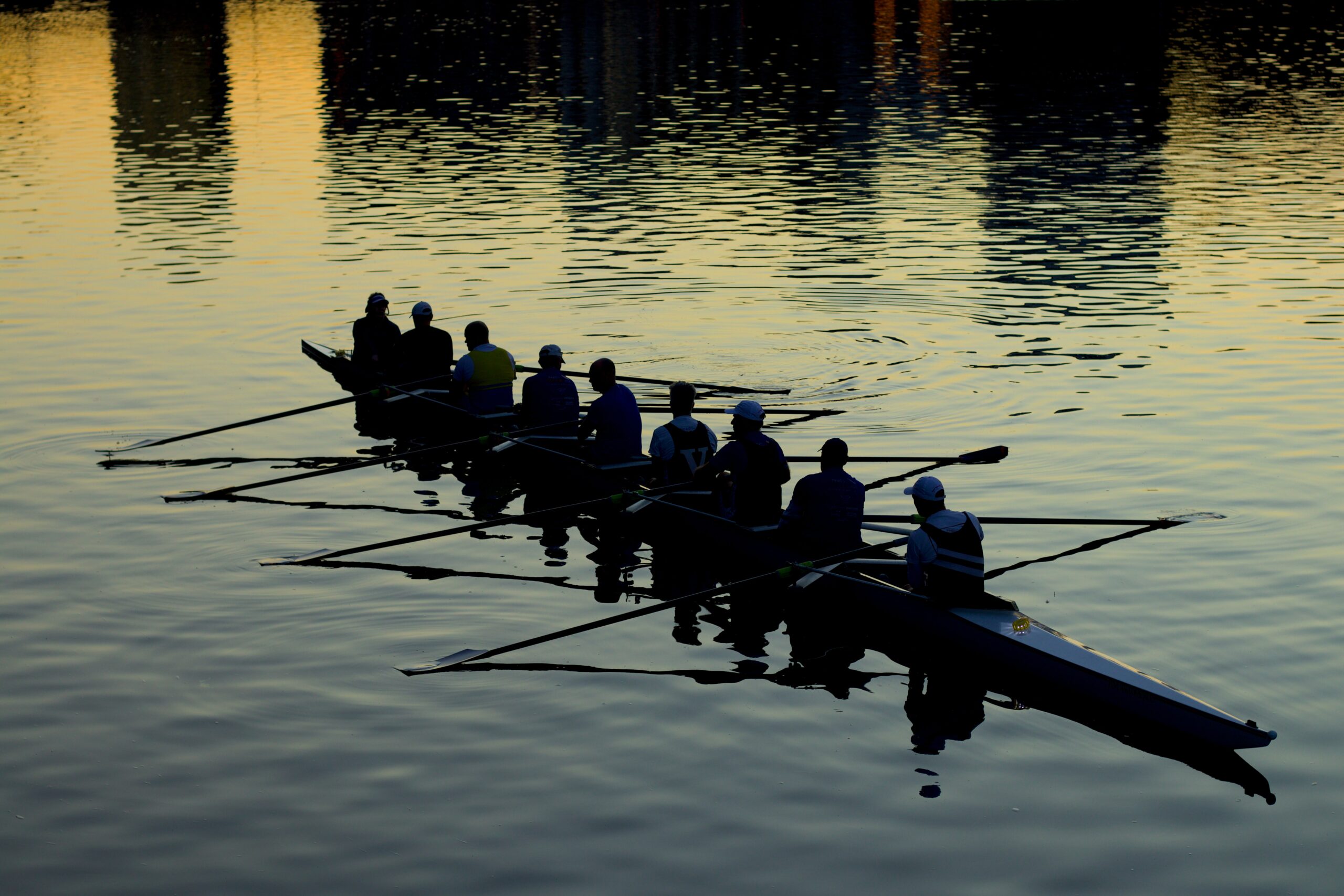 A group of people rowing a canoe on a lake. They are in shadow, as in appears to be the early hours of the morning.