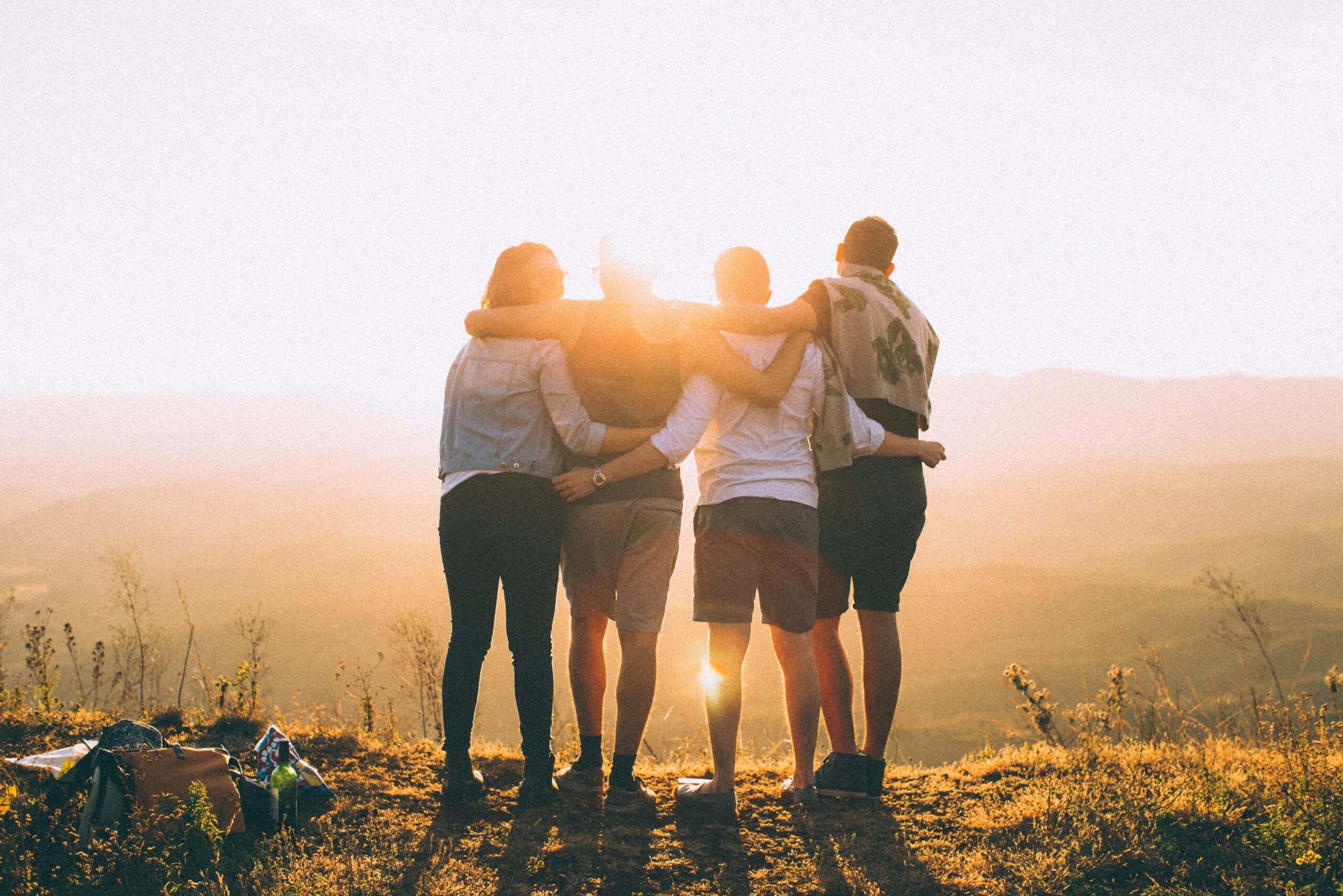 A group of people with their arms around each other, looking at the sunset together.