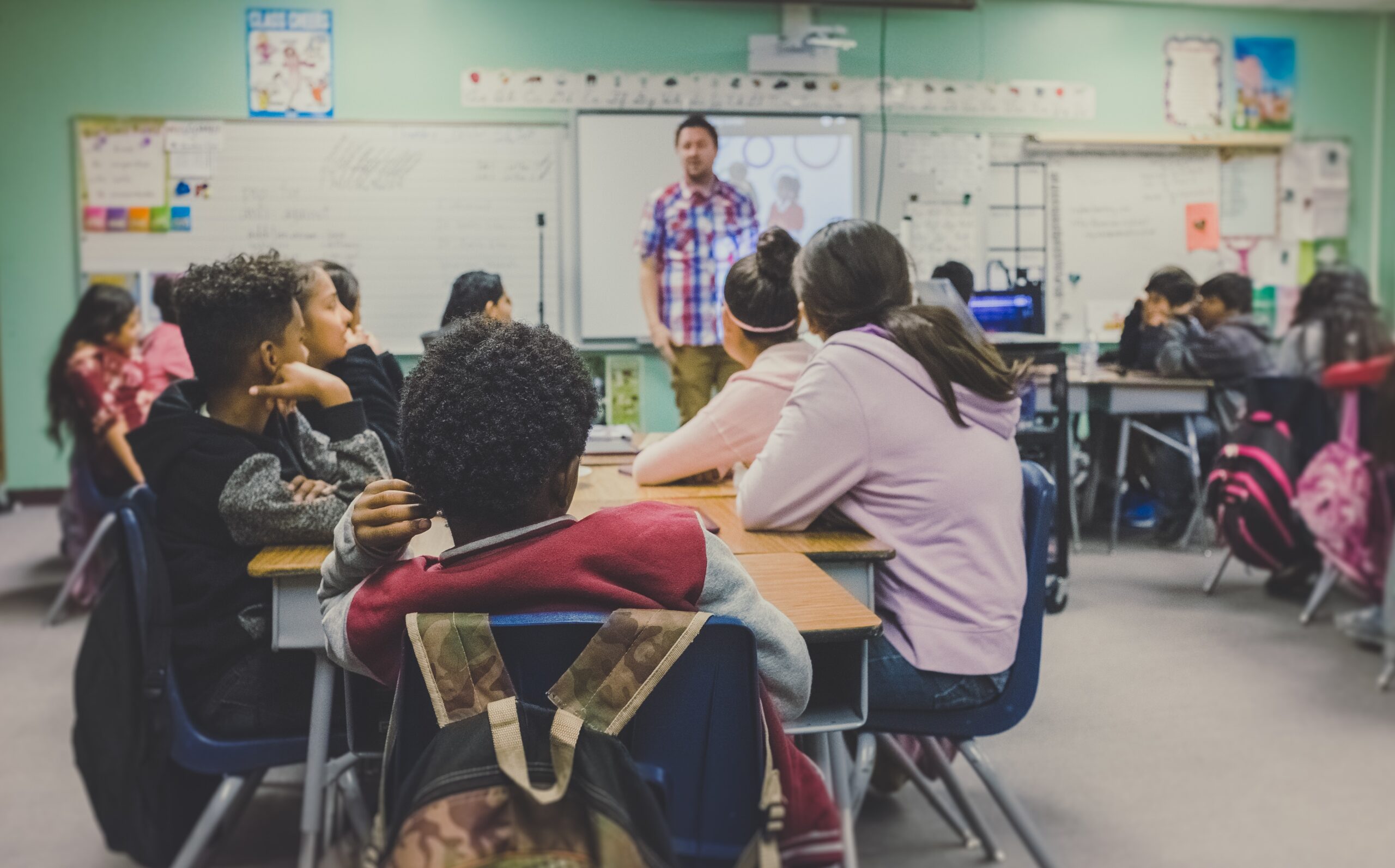 Students in a classroom sitting at their desks looking at the teacher.