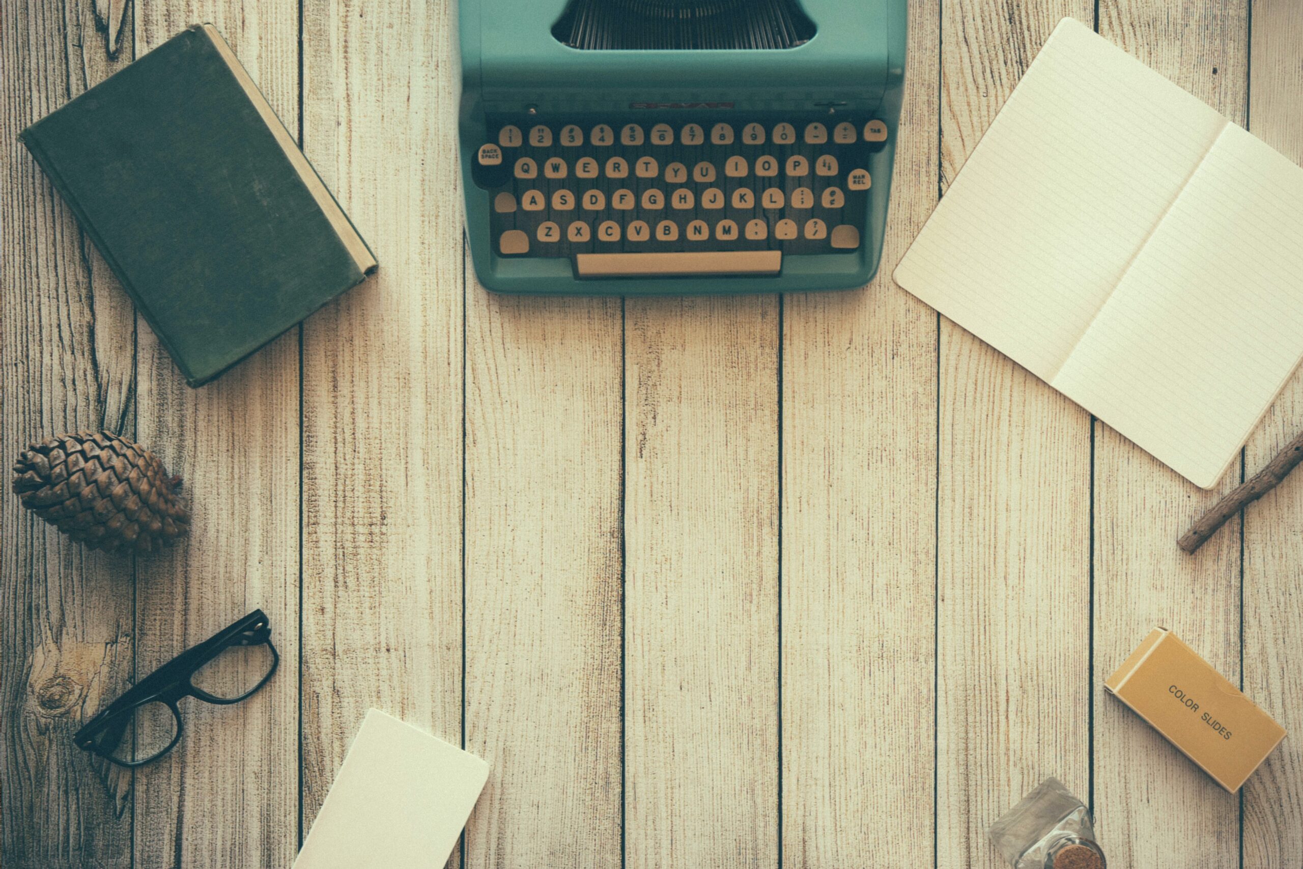 Overhead photo of a desk that has a typewriter, closed book, and an open notepad