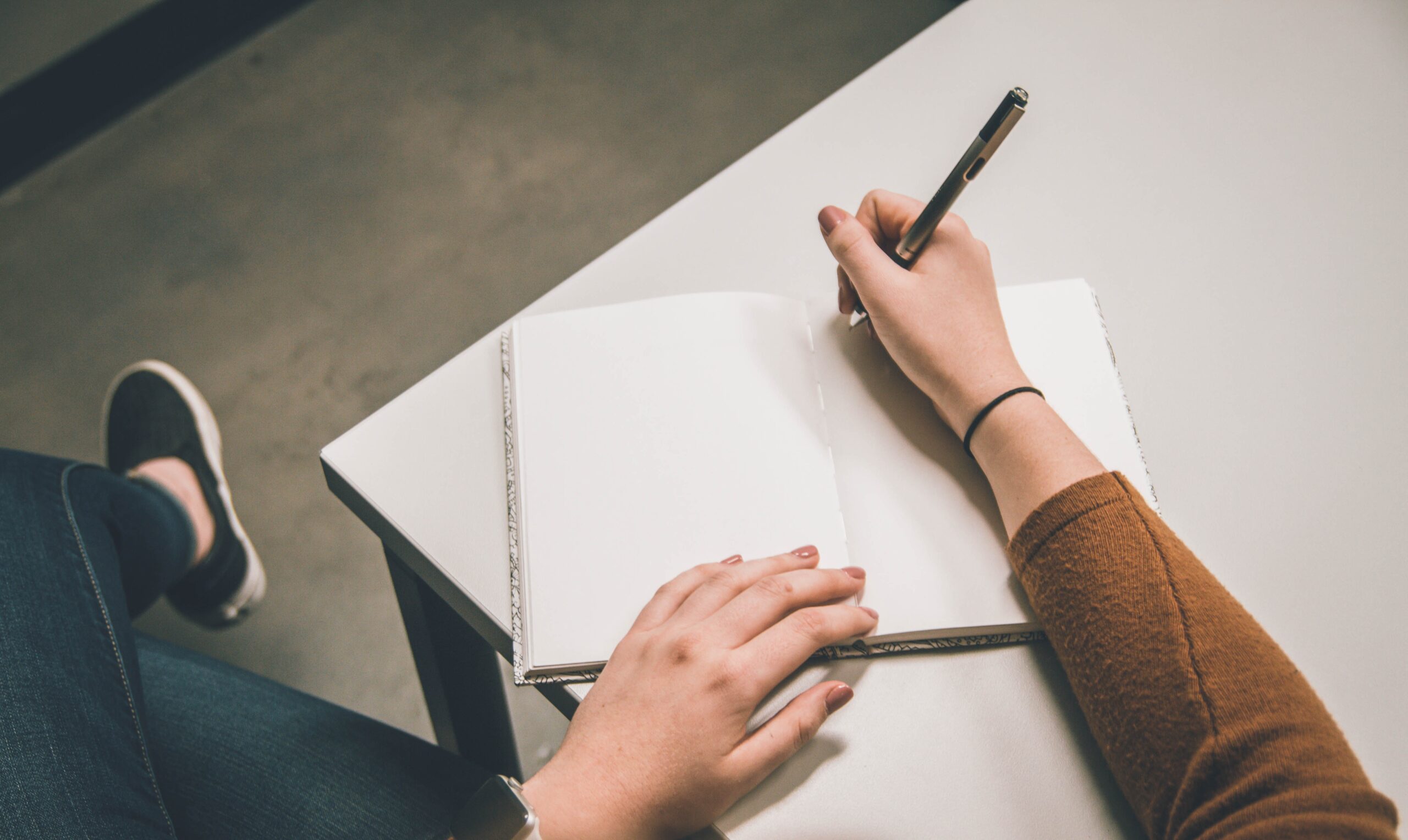 A person with a blank notebook and pen beginning to write.