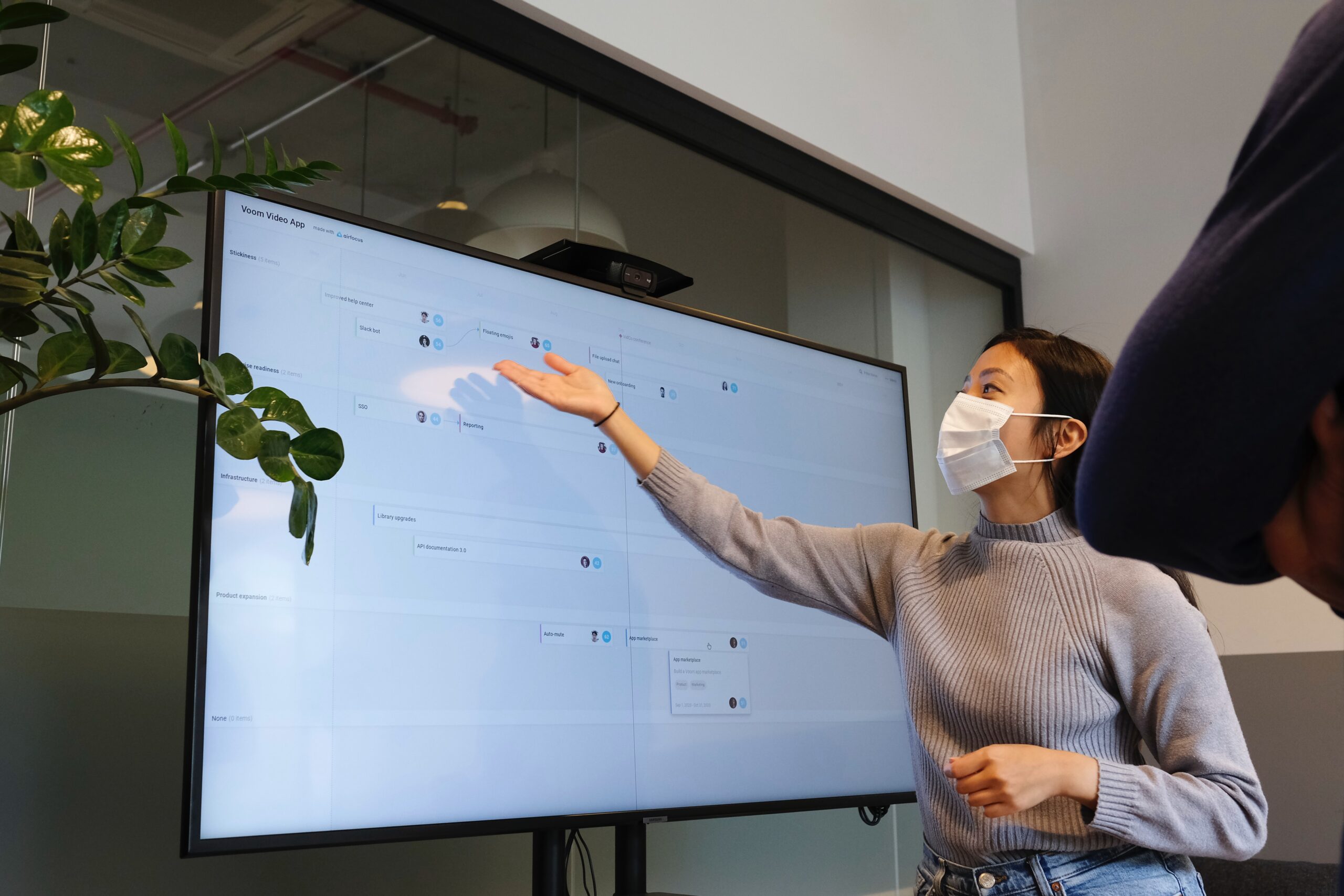 A woman in a mask is standing up to present a board presentation.