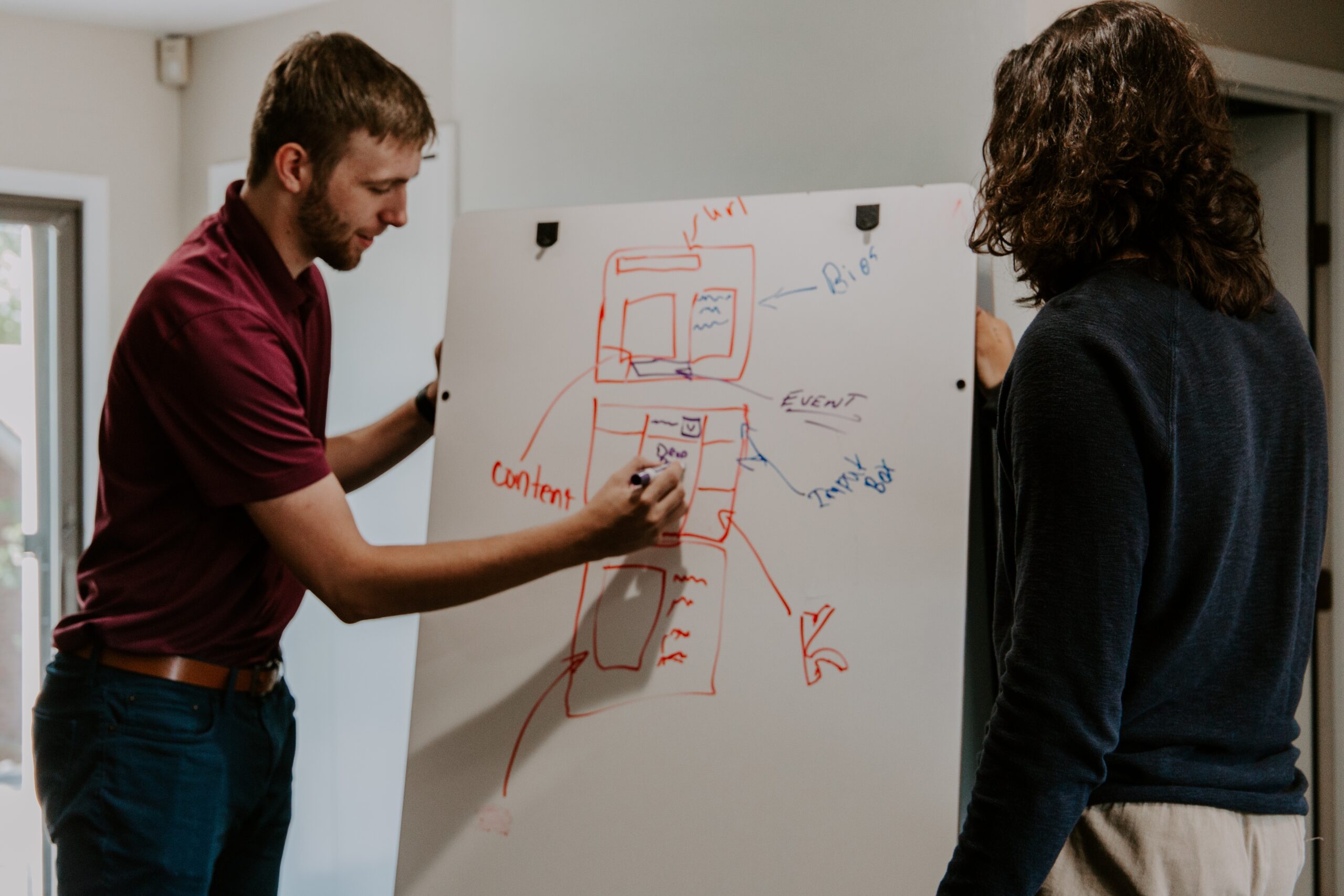 Man drawing model on whiteboard sketching a plan for something and a Woman watching