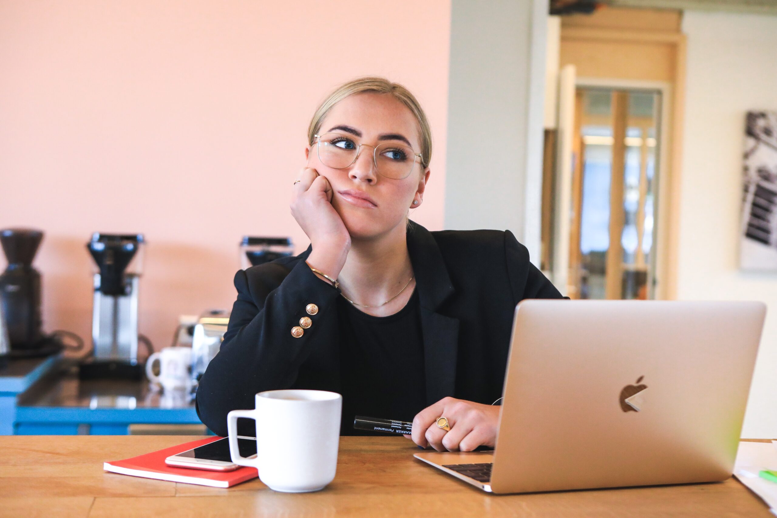 A blonde woman sits in front of her laptop, head propped in hand, and staring to the side.