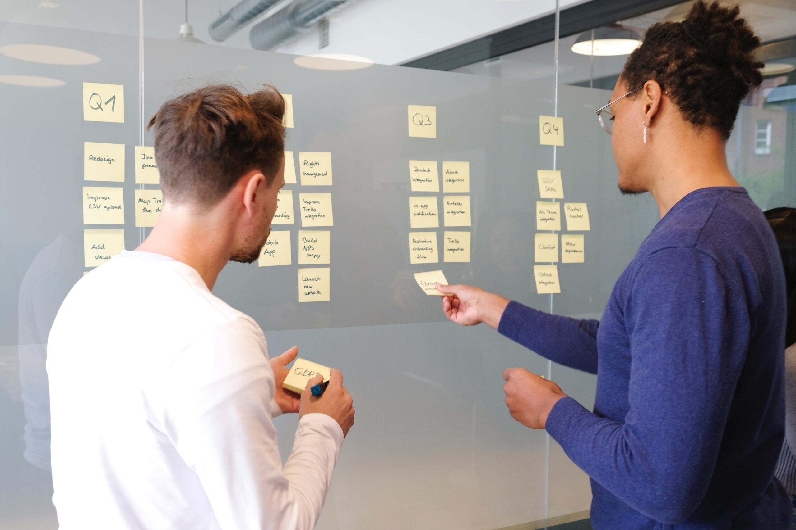 two guys in front of a window reviewing ideas on post it notes