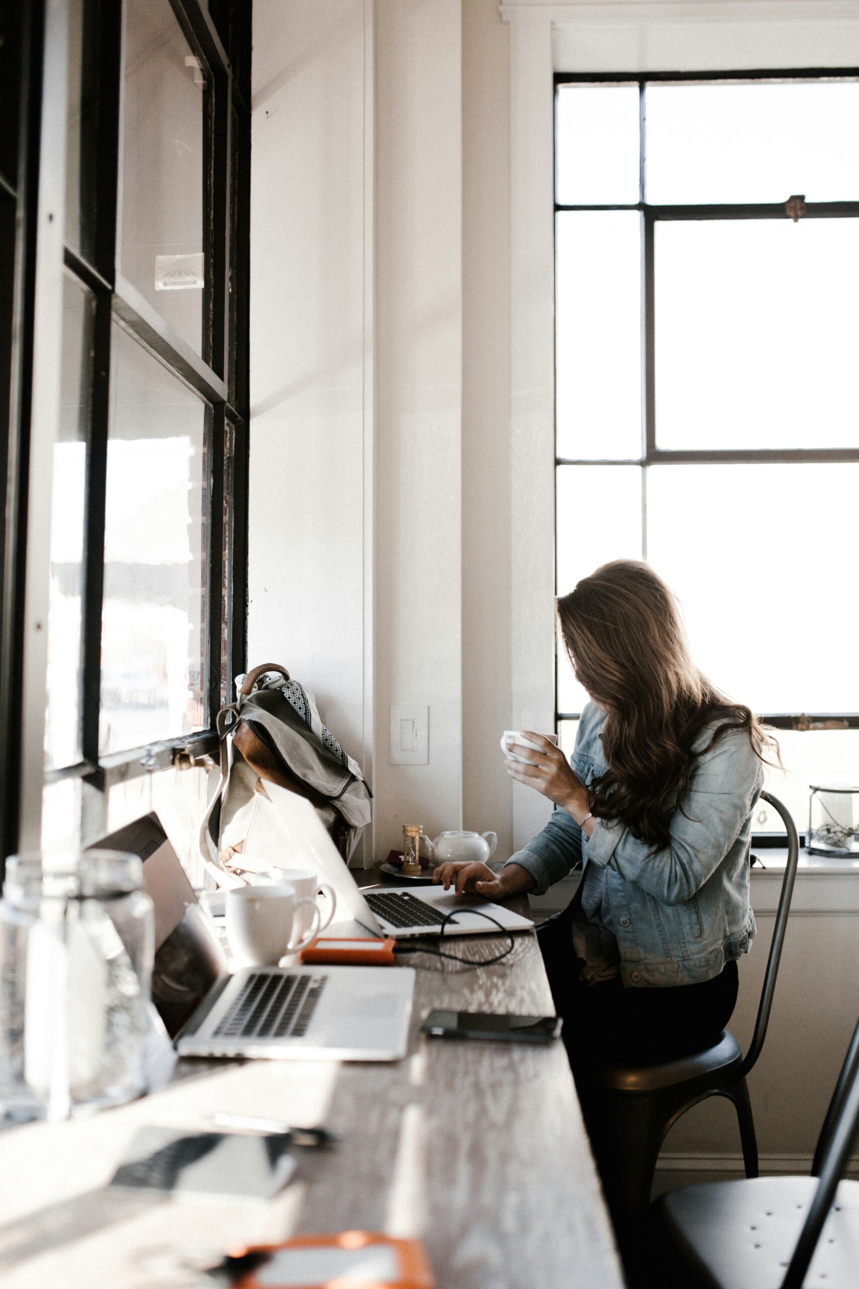 A woman is drinking coffee while surrounded by computers and wires.