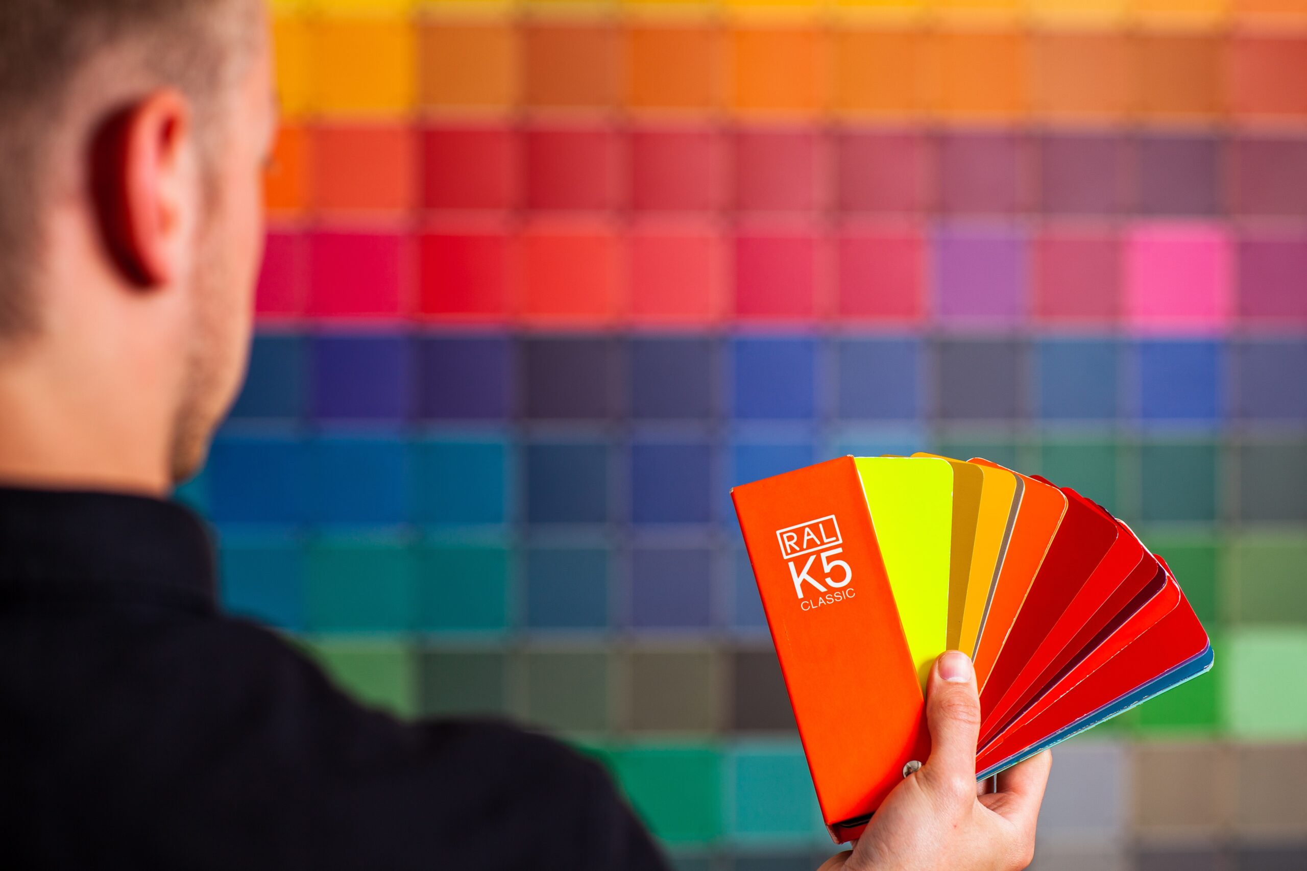 man in front of a wall of color swatches, while holding different red shades on his hand