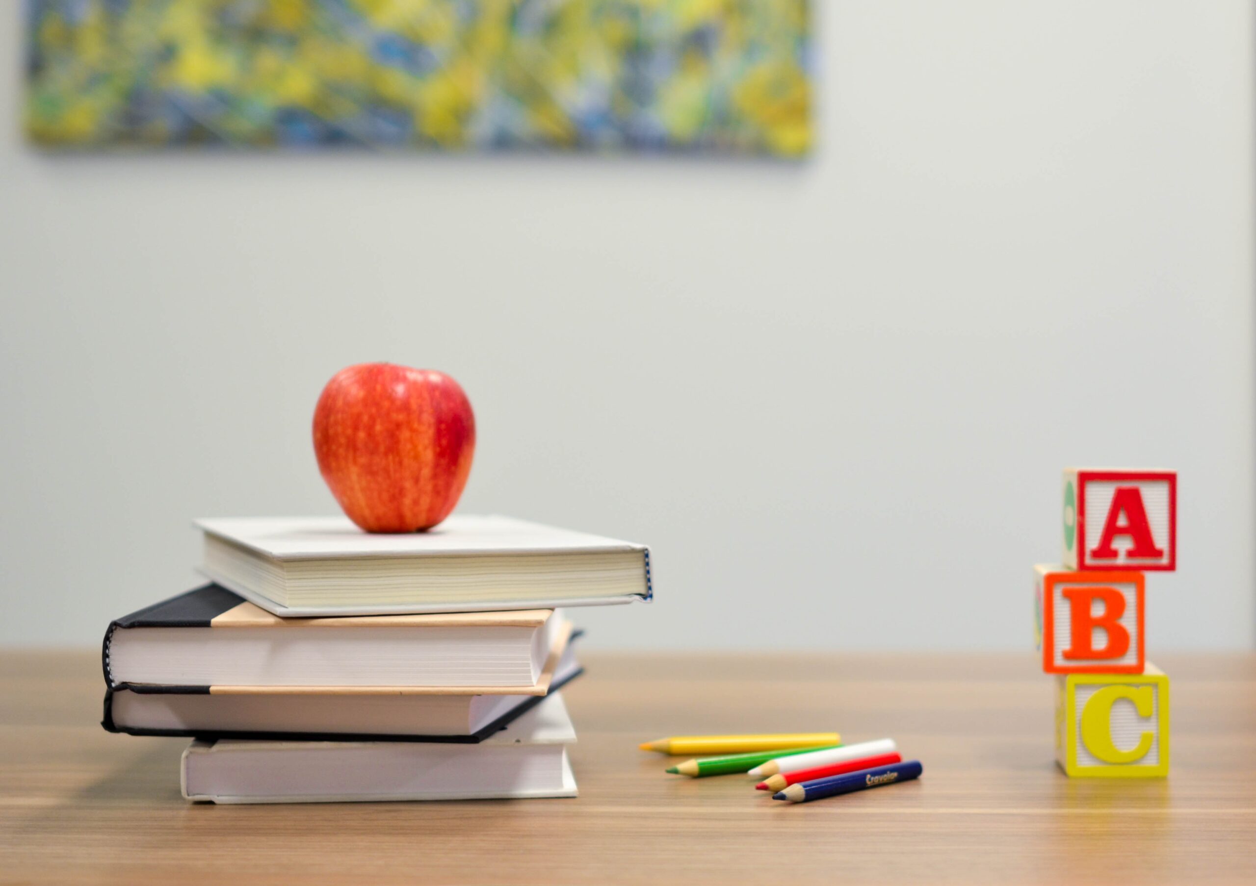 a desk with books, an apple, colored pencils and blocks that spell ABC.