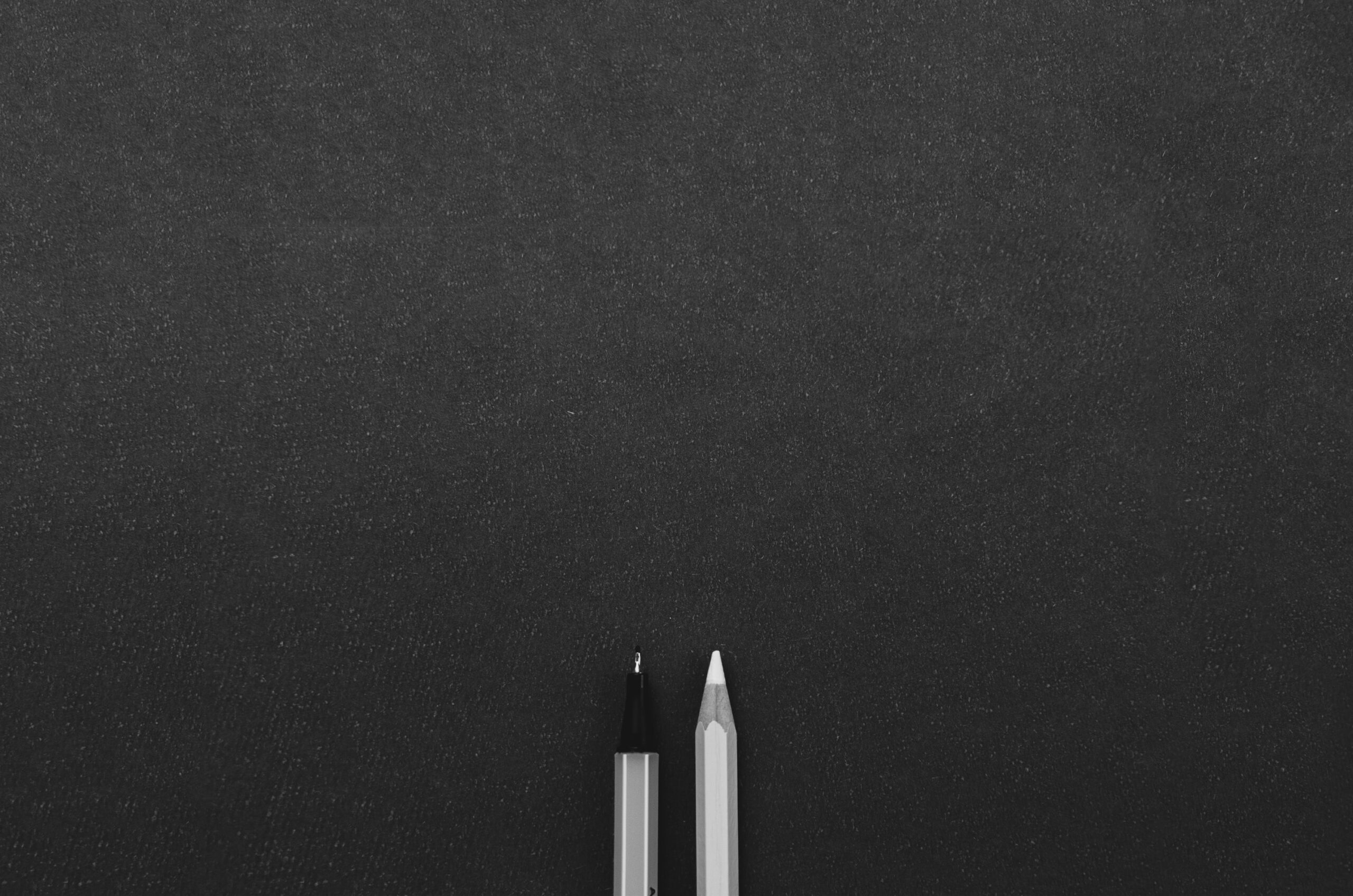 A pen and pencil sitting on top of a black surface