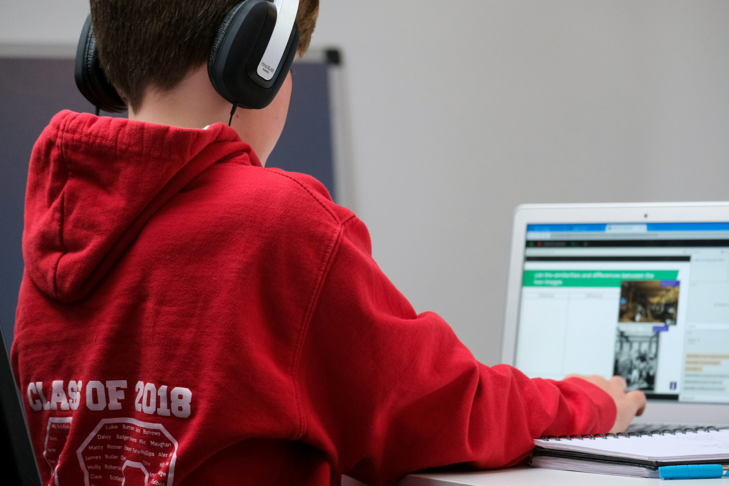 Image of a child sitting at a computer with headphones on and a notebook near him.