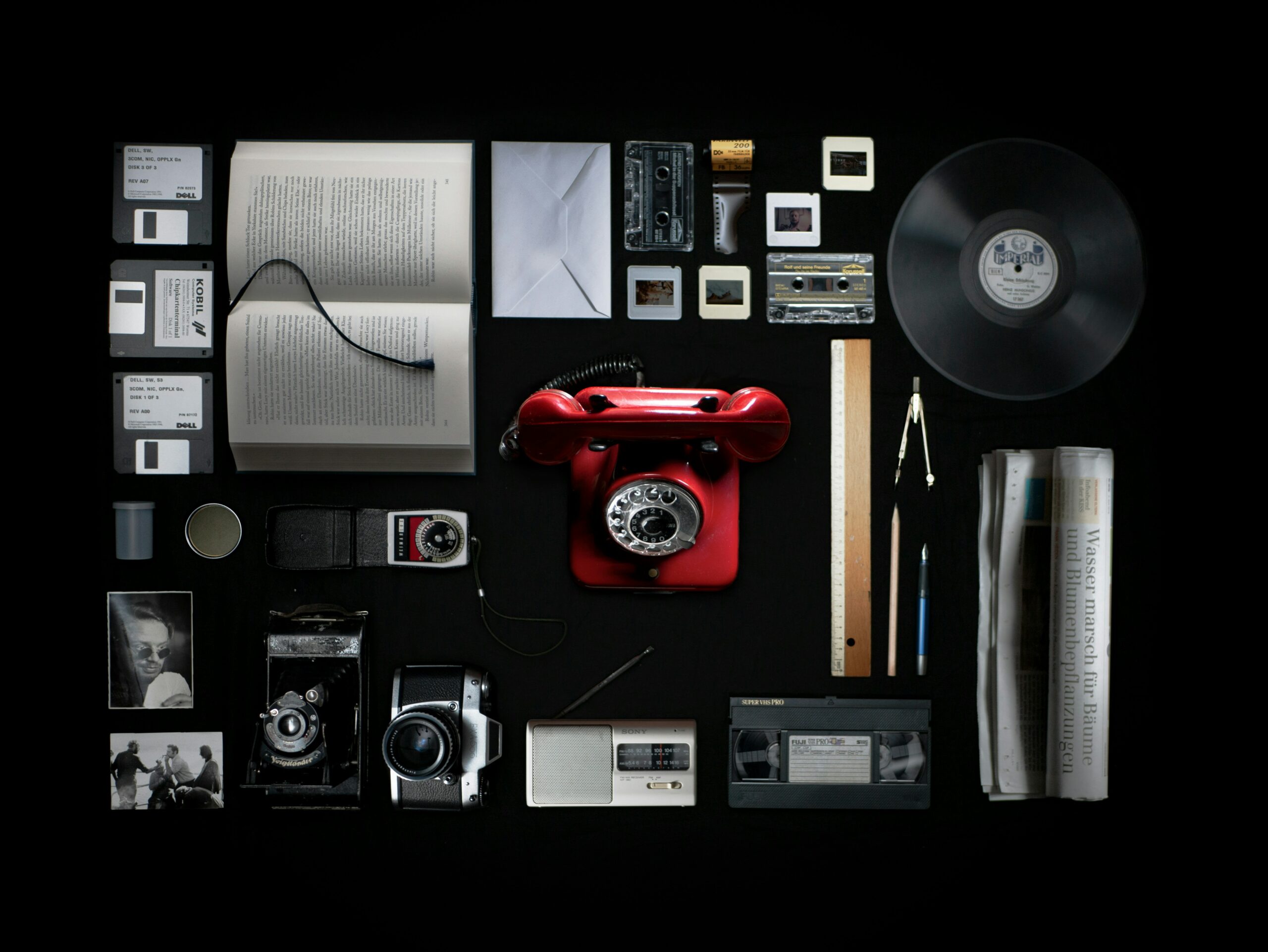 A photo of various forms of technology and digital media used for communication, such as a phone, book, letter, camera, tape etc.
