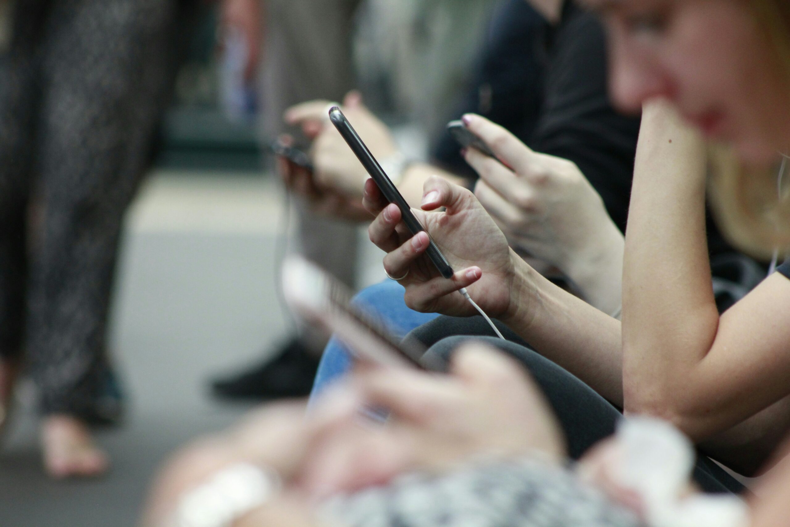 The photo depicts multiple people out in public with their phones in their hands.