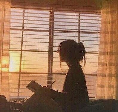 A woman sitting in front of a window writing in a journal during golden hour