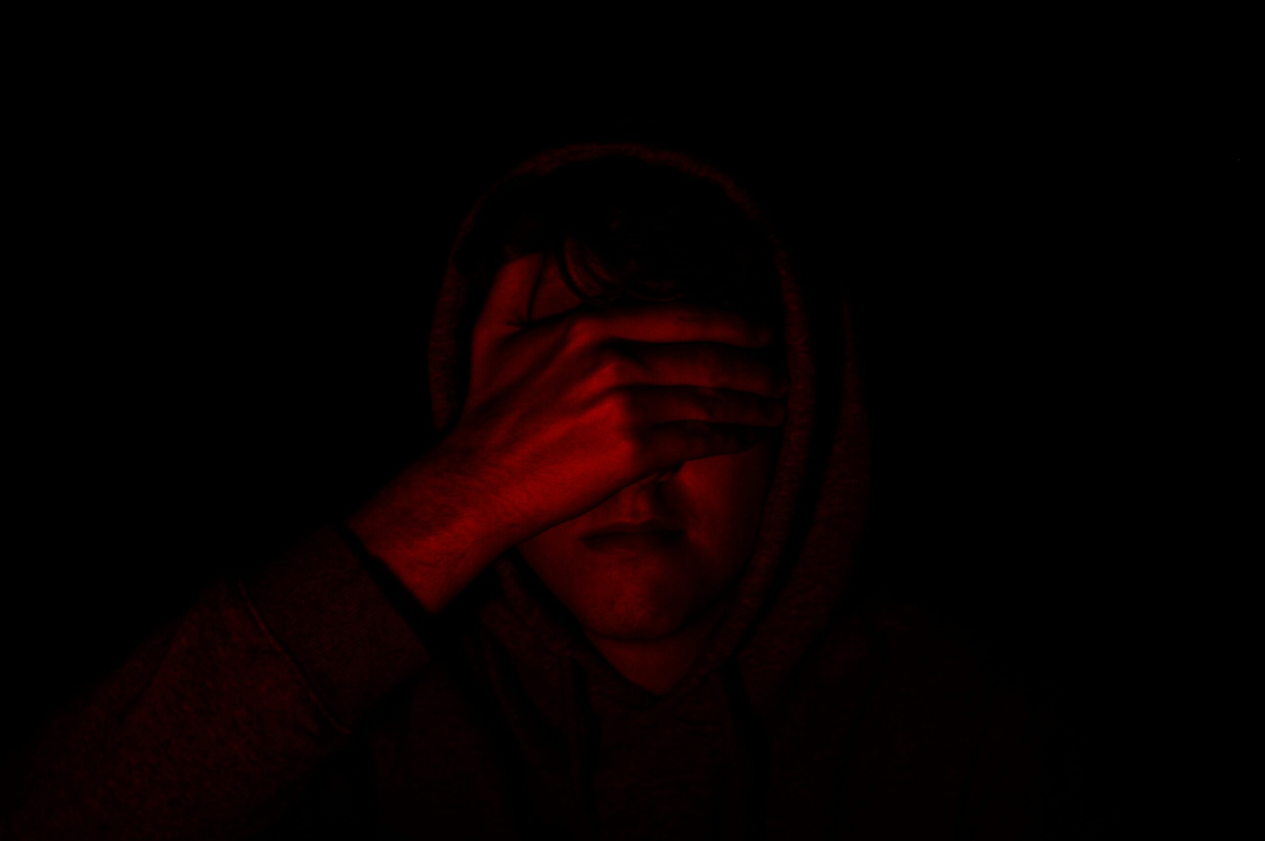 A girl covering her face with her hand in very dark red lighting.