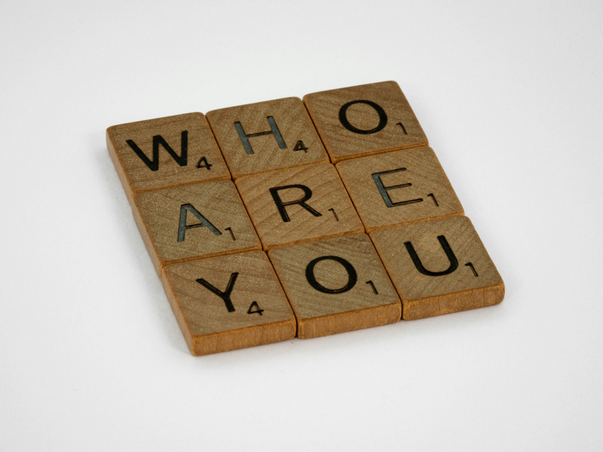 Six scrabble pieces are placed together to form the question "Who Are You"