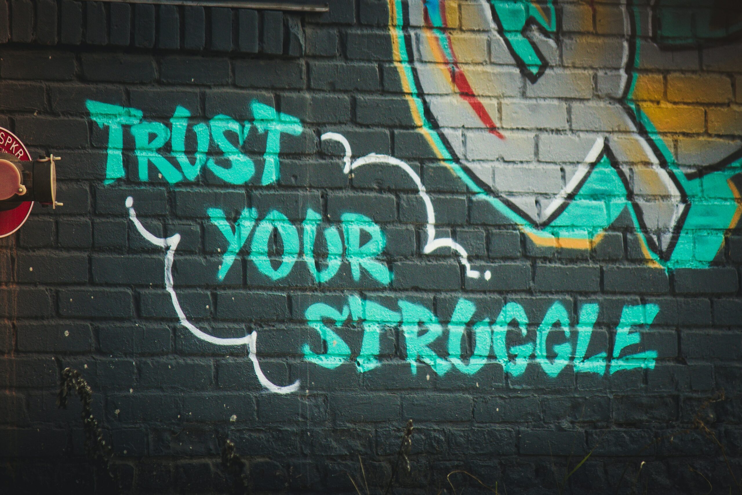 Graffiti of blue text that reads "Trust Your Struggle"