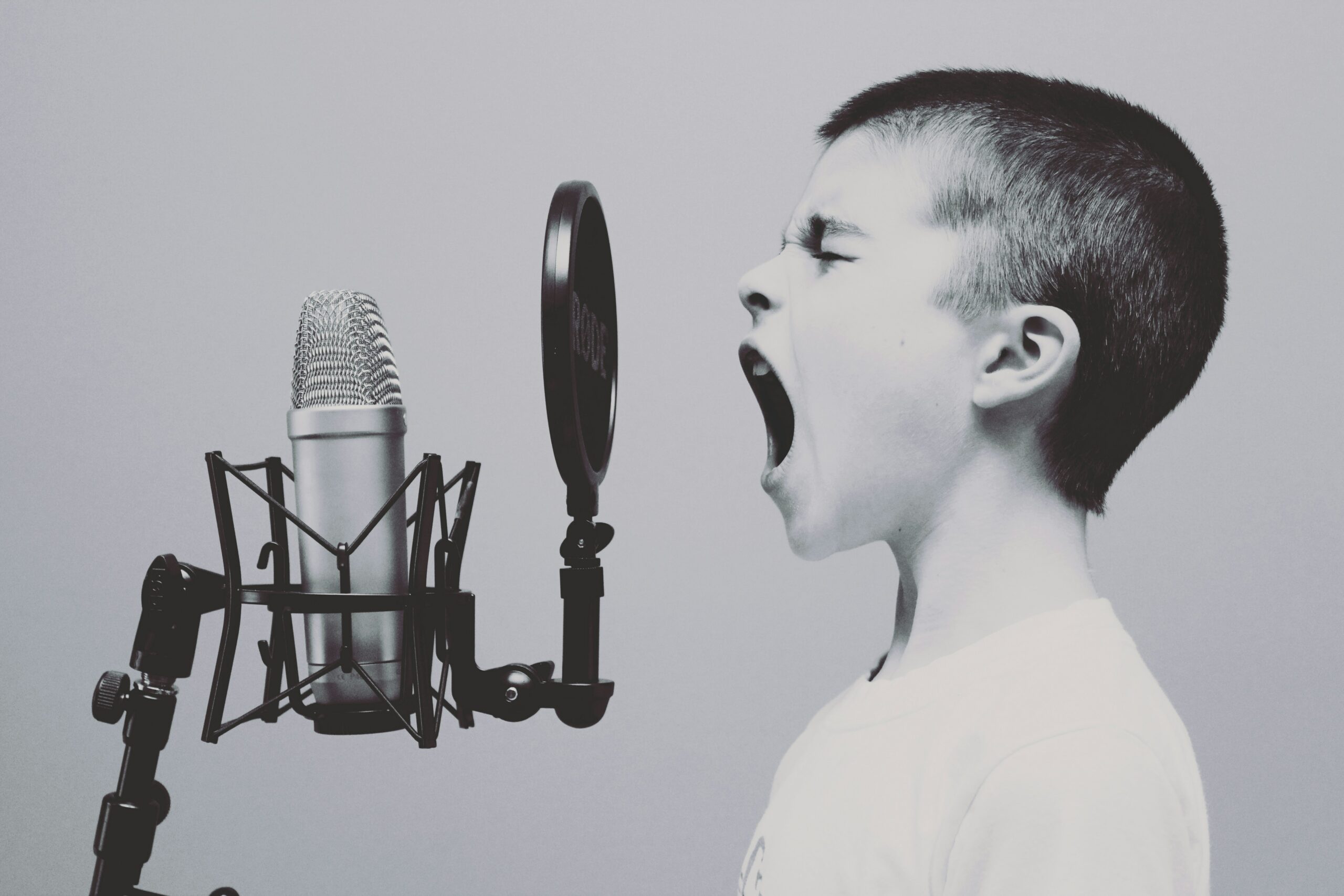 Black and white image of boy screaming into recording microphone.