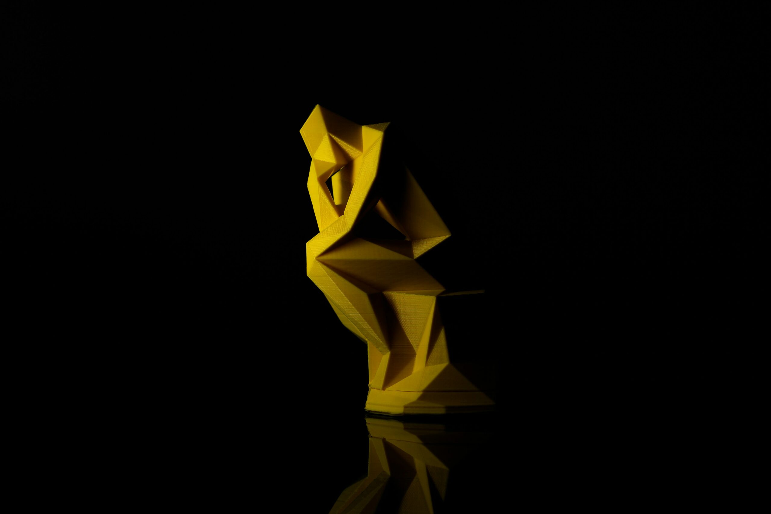 a little yellow sculpture that resembles 'the thinker' while it sits alone in the dark