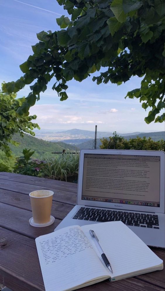 sitting at a table with outside scenery with a coffee, a journal and a laptop