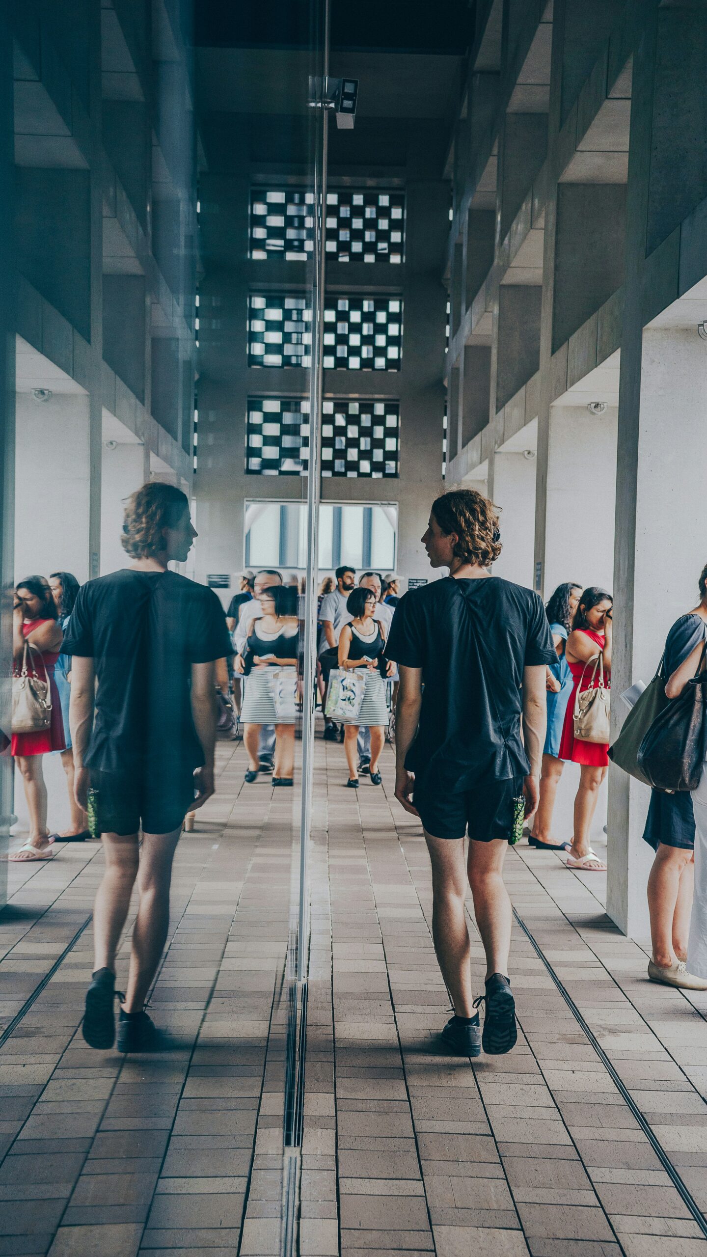 Person walking towards a crowd looking at their reflection in a mirror wall