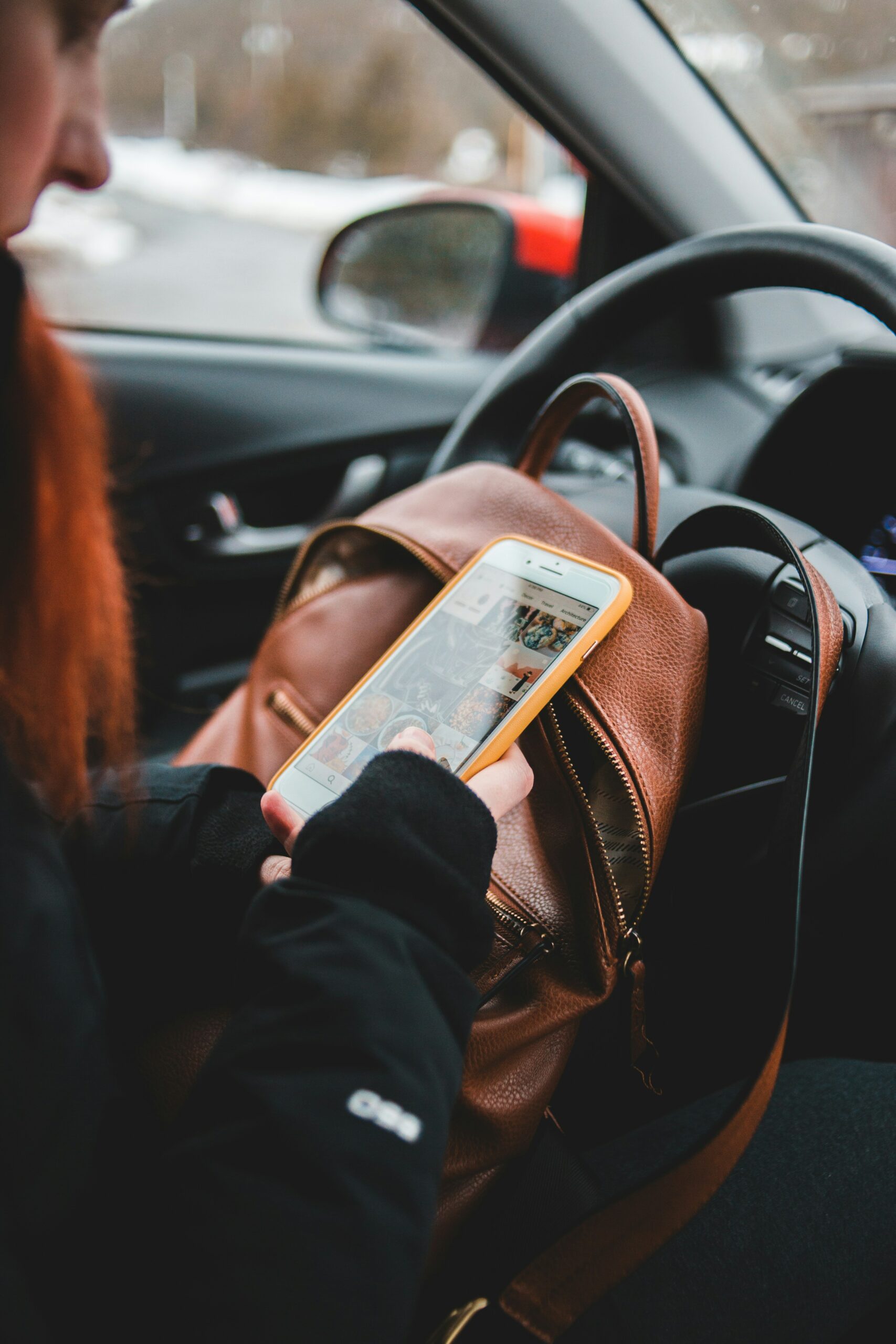 A woman is in her car, and she is on her phone presumably texting someone.