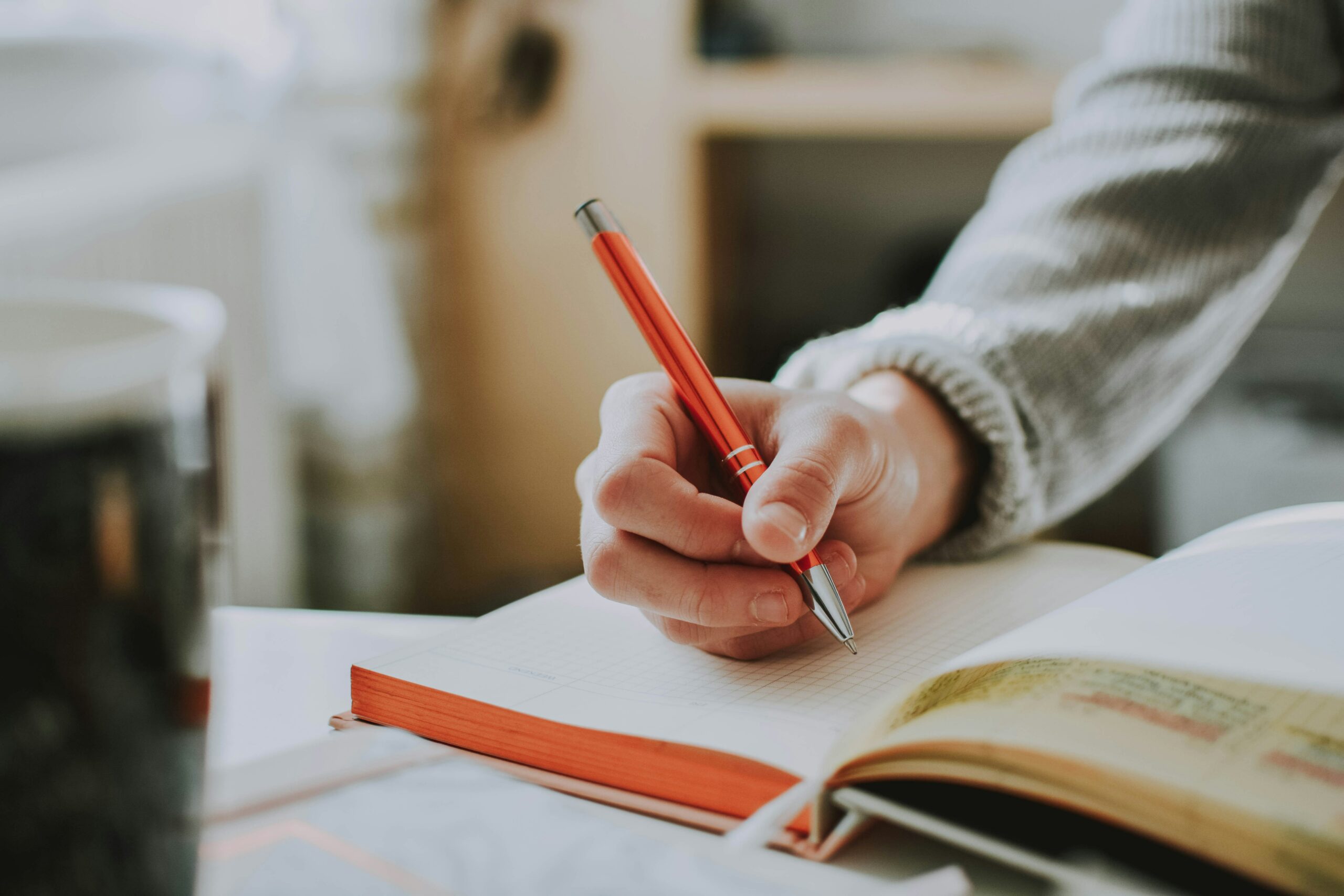 Photo of someone writing in a notebook with a pen.