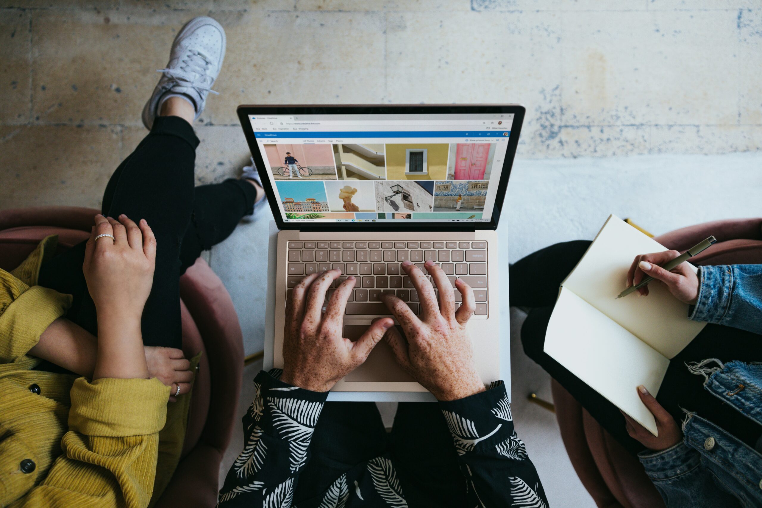 Photo of three people sitting around a laptop, one with a notebook and pen in hand.