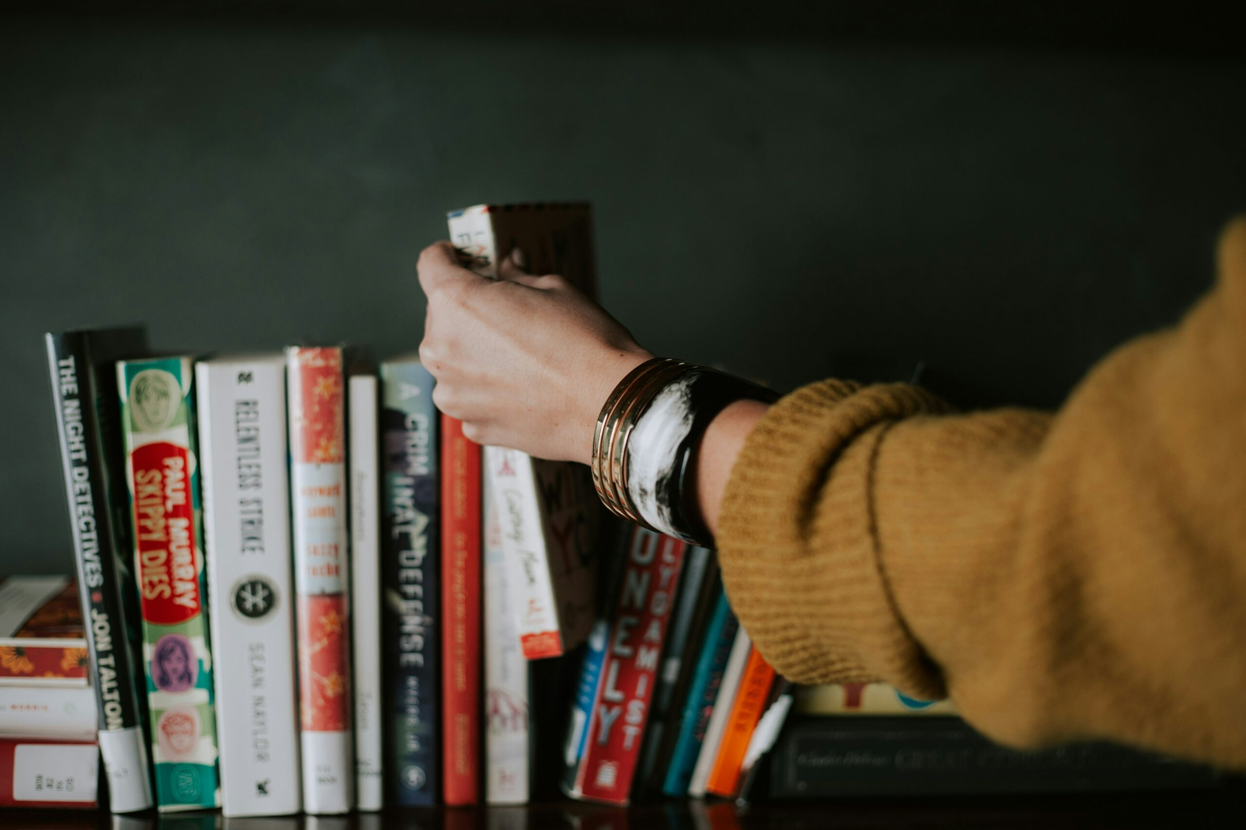 Photo of a person's arm reaching for a book on a bookshelf.