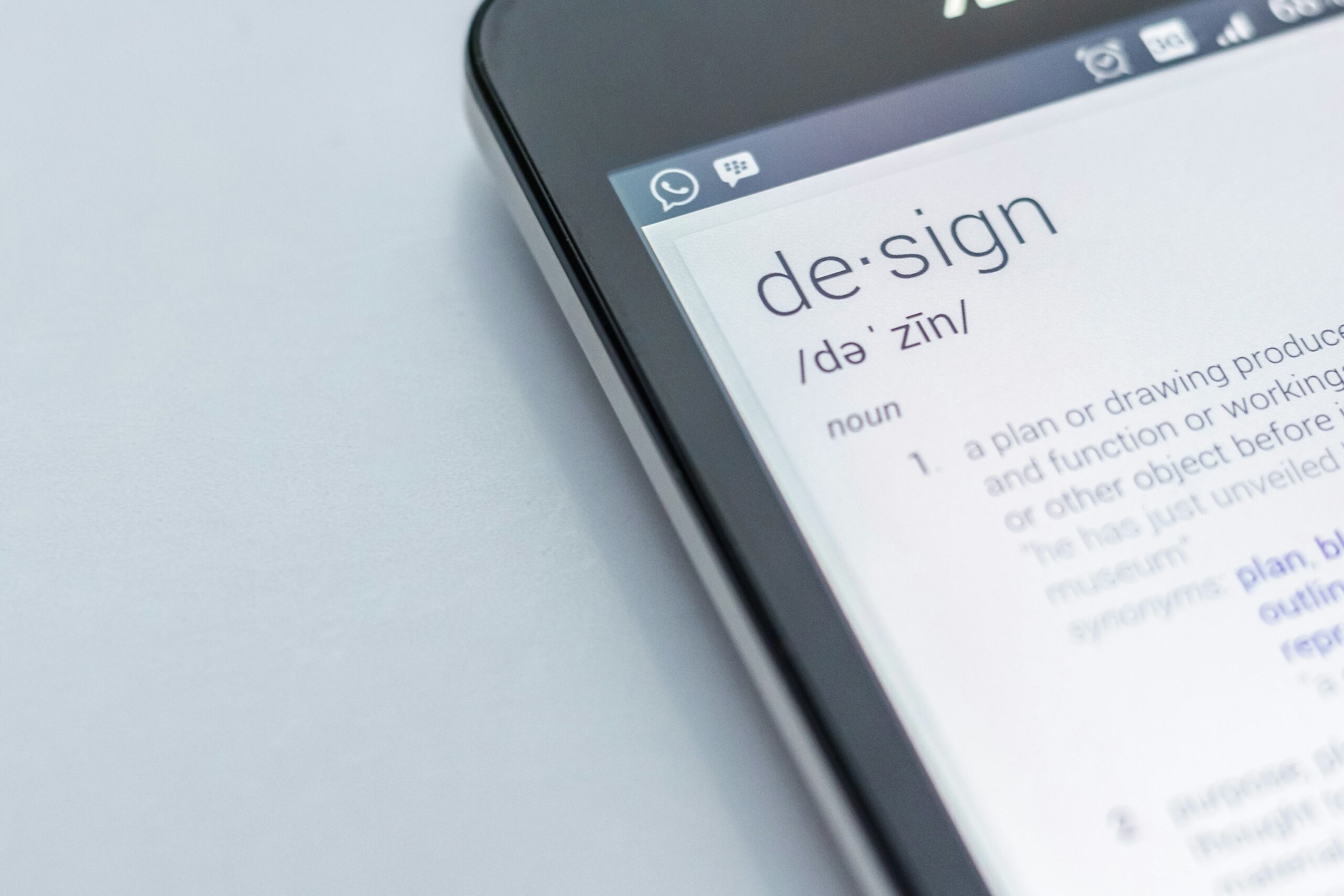 A phone shows the word design and its definition.