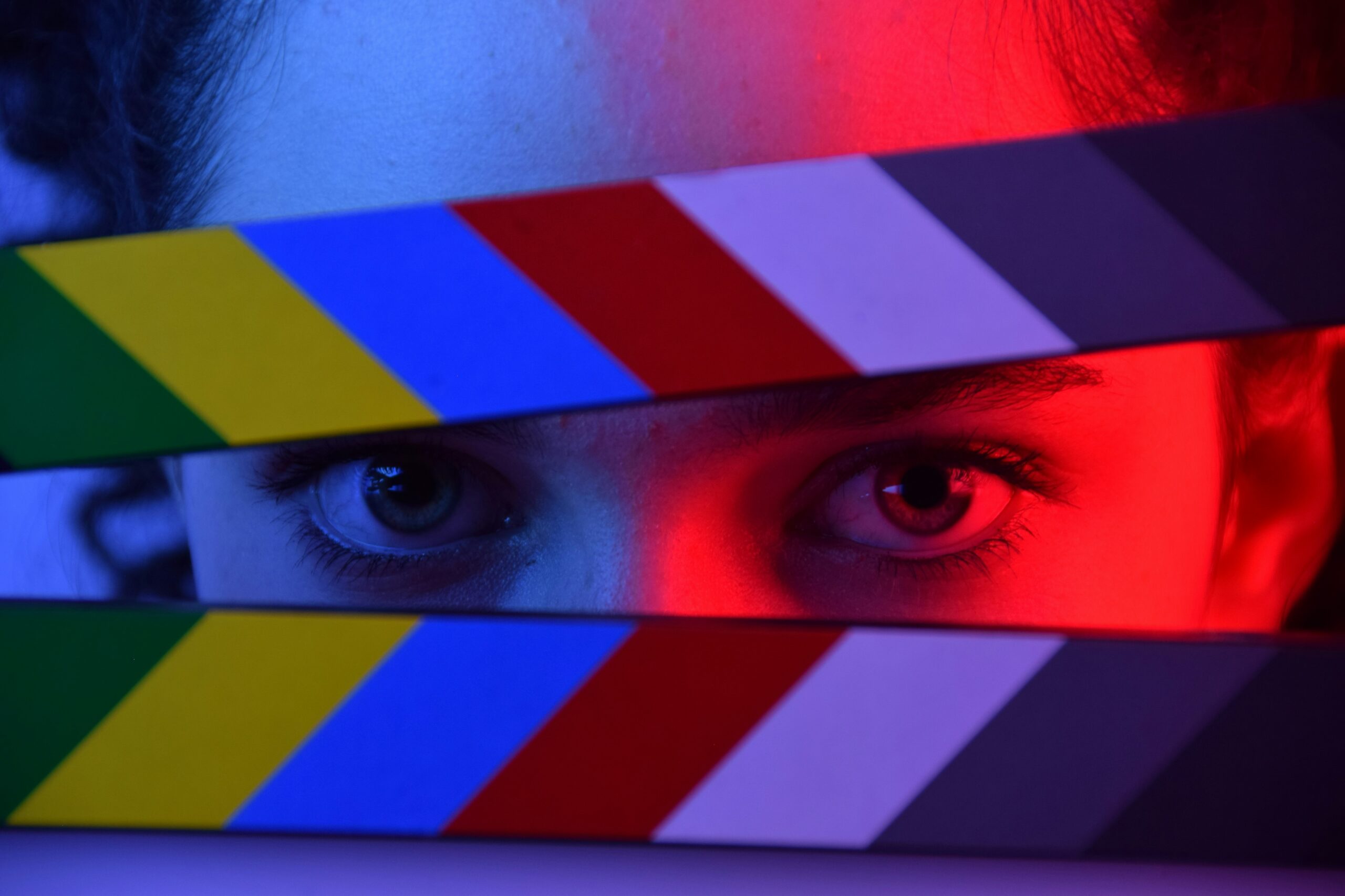 There is a woman behind a movie clapperboard that is slightly opened to only show her eyes