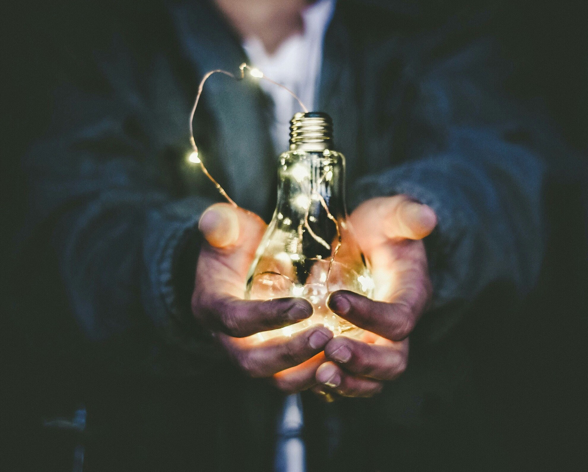 two hands holding a string of lights inside a lightbulb