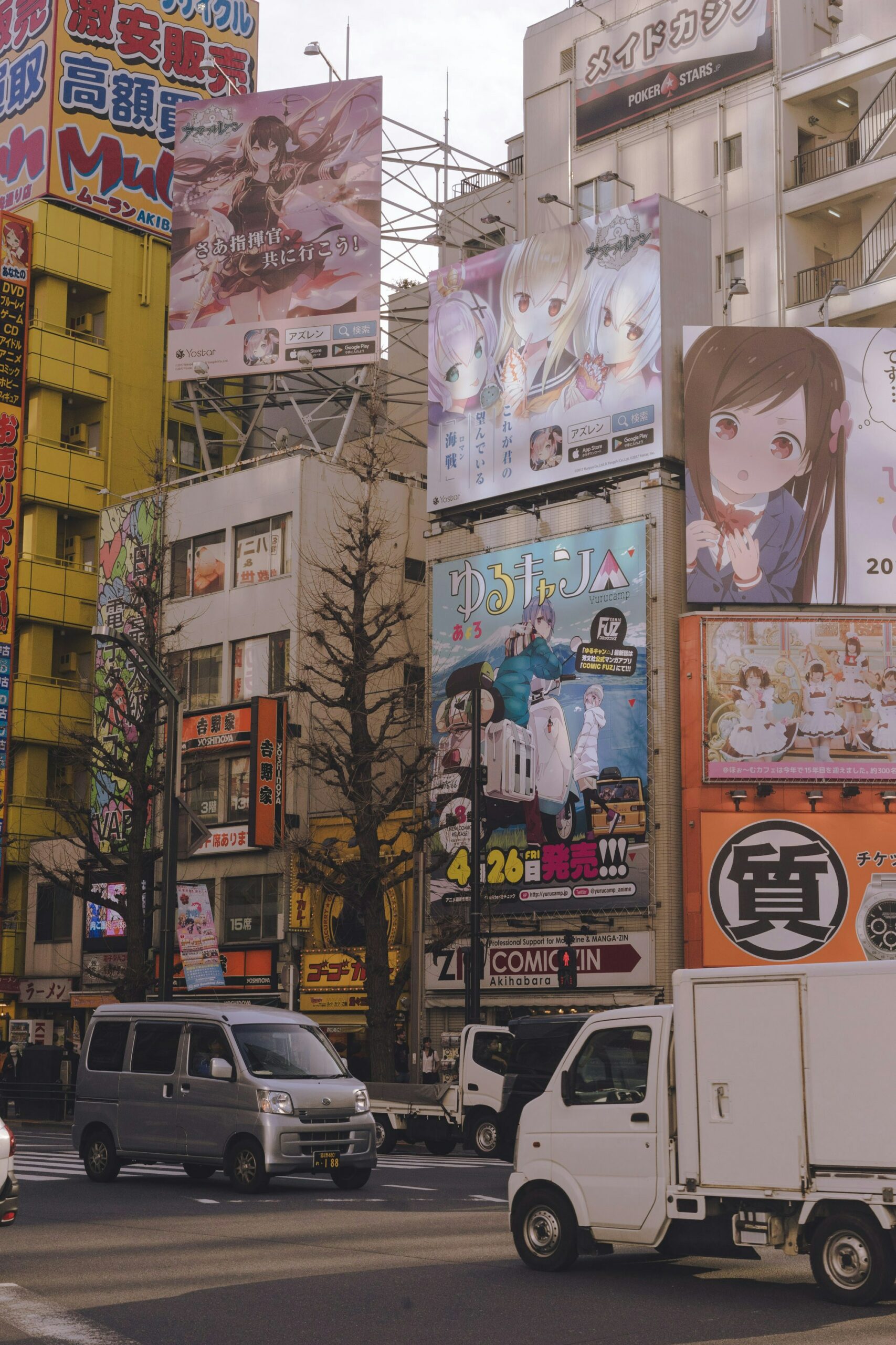 A corner with multiple apartments built close together, each having at least one giant poster in Japanese of an anime plastered on it.