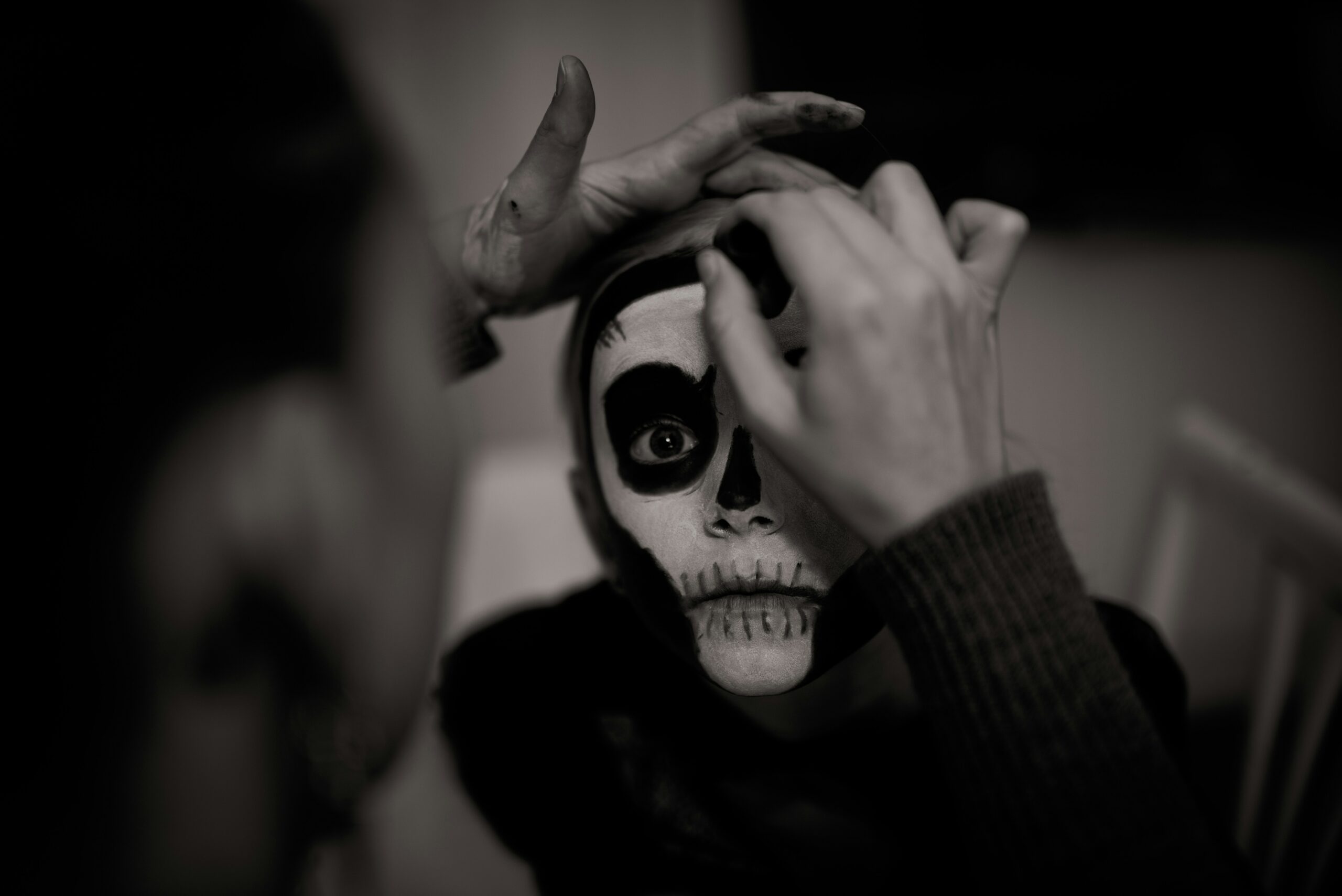 Black and white photo of someone painting on skeleton makeup on a child's face.