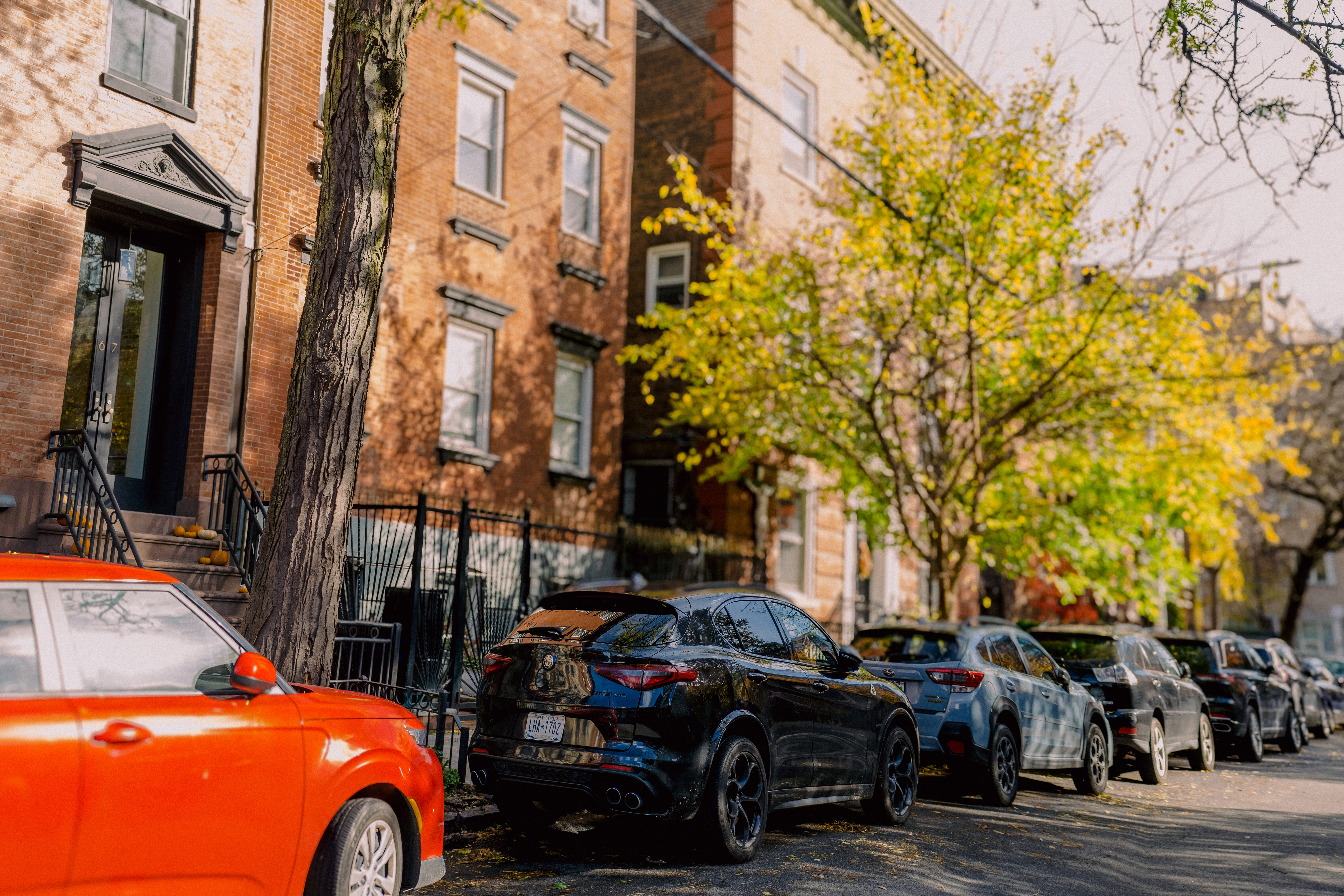 Photo of a wealthy UES street. Shows a row of townhouses and expensive cars.