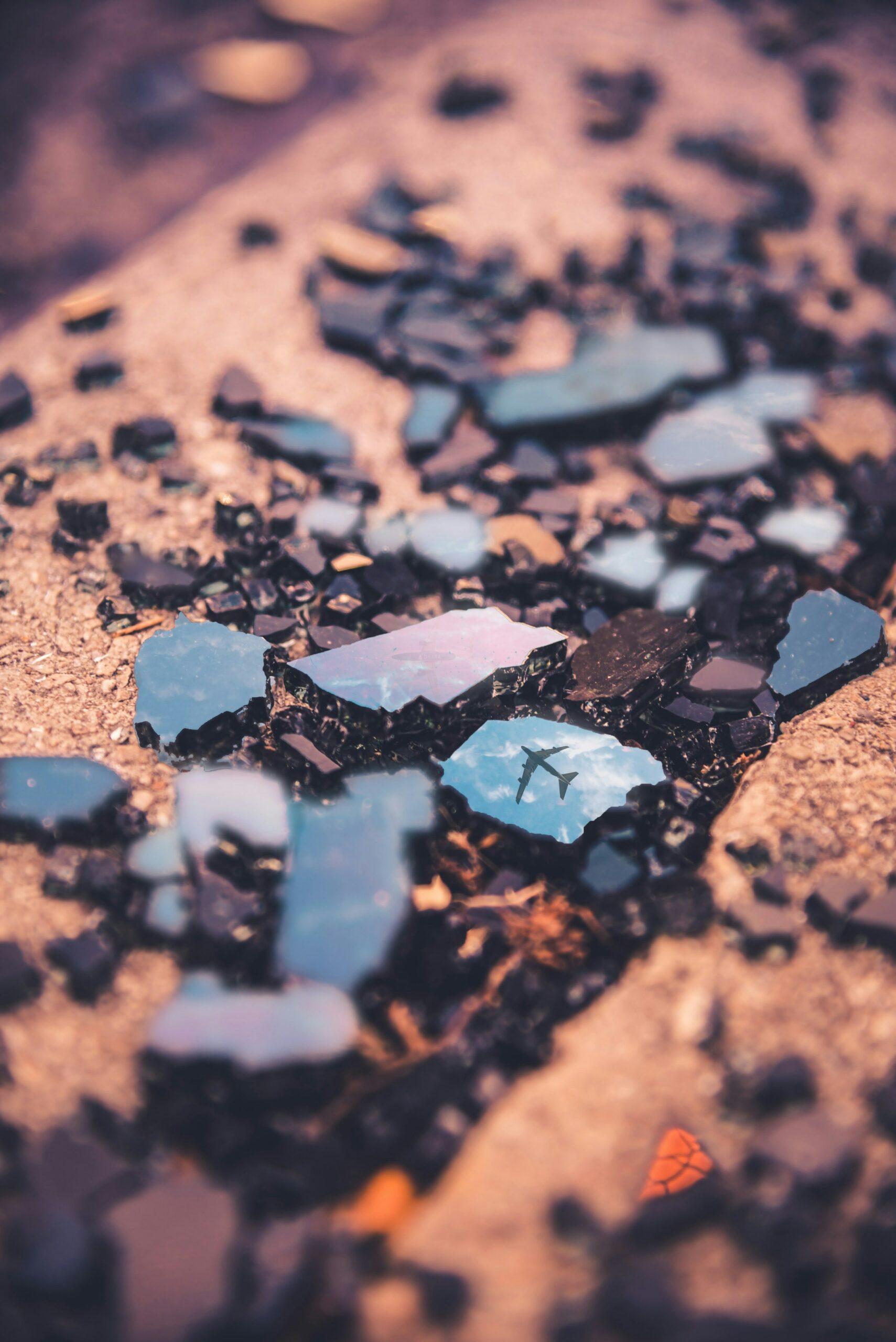 The shards of something resembling black rocks lay across a red, dry terrain. In one of the shards is the reflection of an airplane.